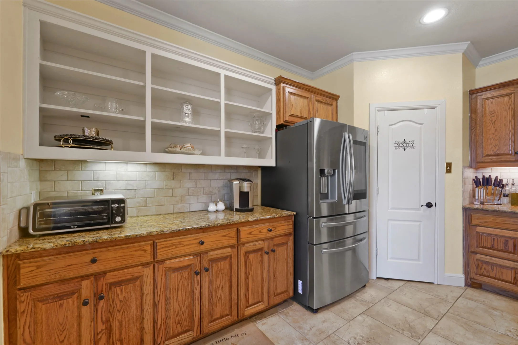 Granite countertops, subway tile backsplash, custom wood cabinetry, open shelving, and tiled flooring