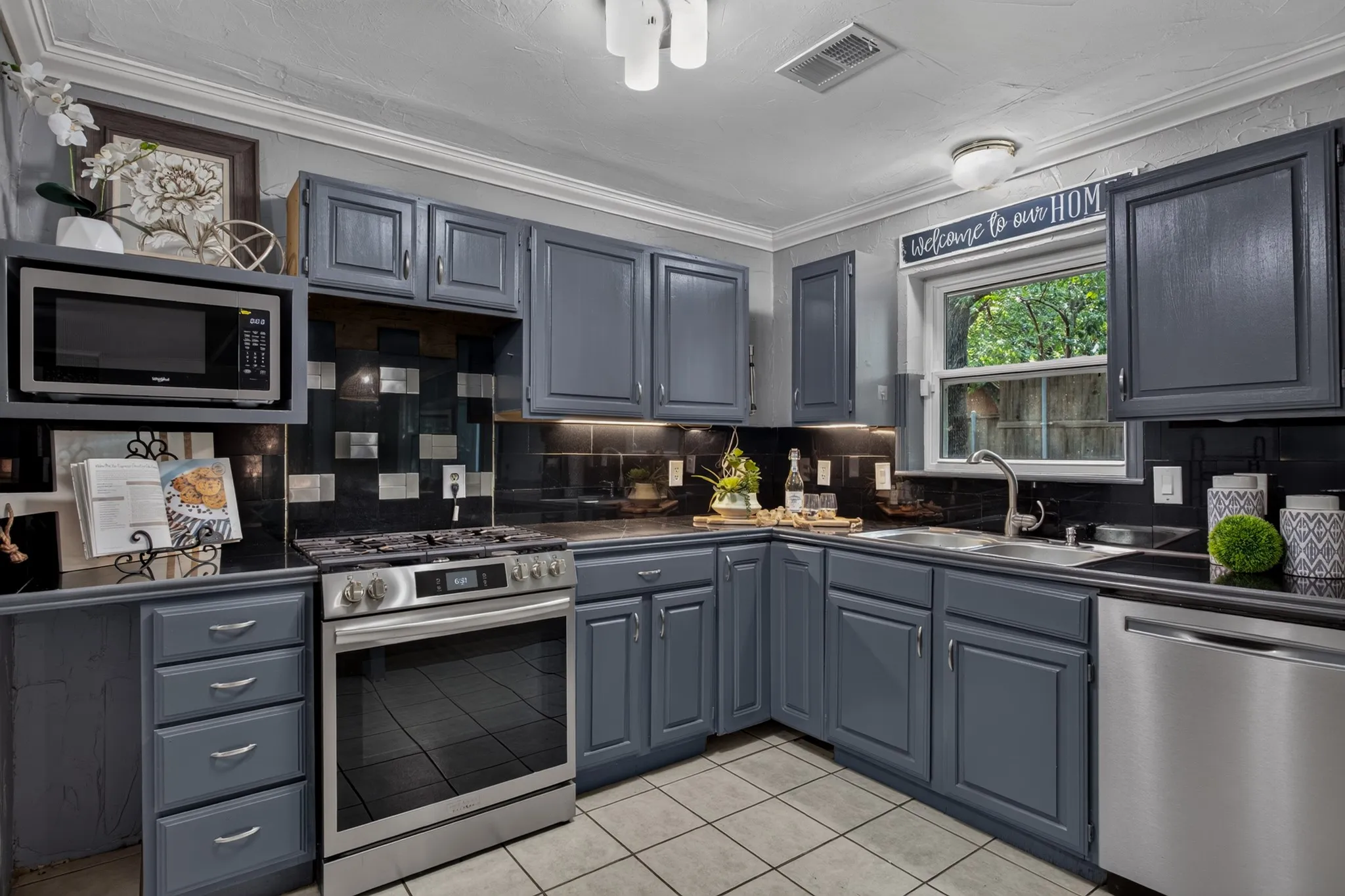 The kitchen is designed for gathering with gray cabinetry, tile countertops and backsplash, stainless steel appliances and gas cooktop, a Frigidaire dishwasher and a refrigerator that conveys with the home. A space perfect for moving in and enjoying or customizing it to make it your own.