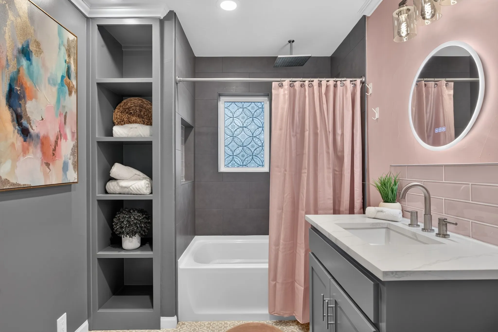 The third full bath, close to bed #3 is pretty in pink with pink glass subway tile accents, backlit mirror, charcoal designer tile surround with rain shower and built ins.