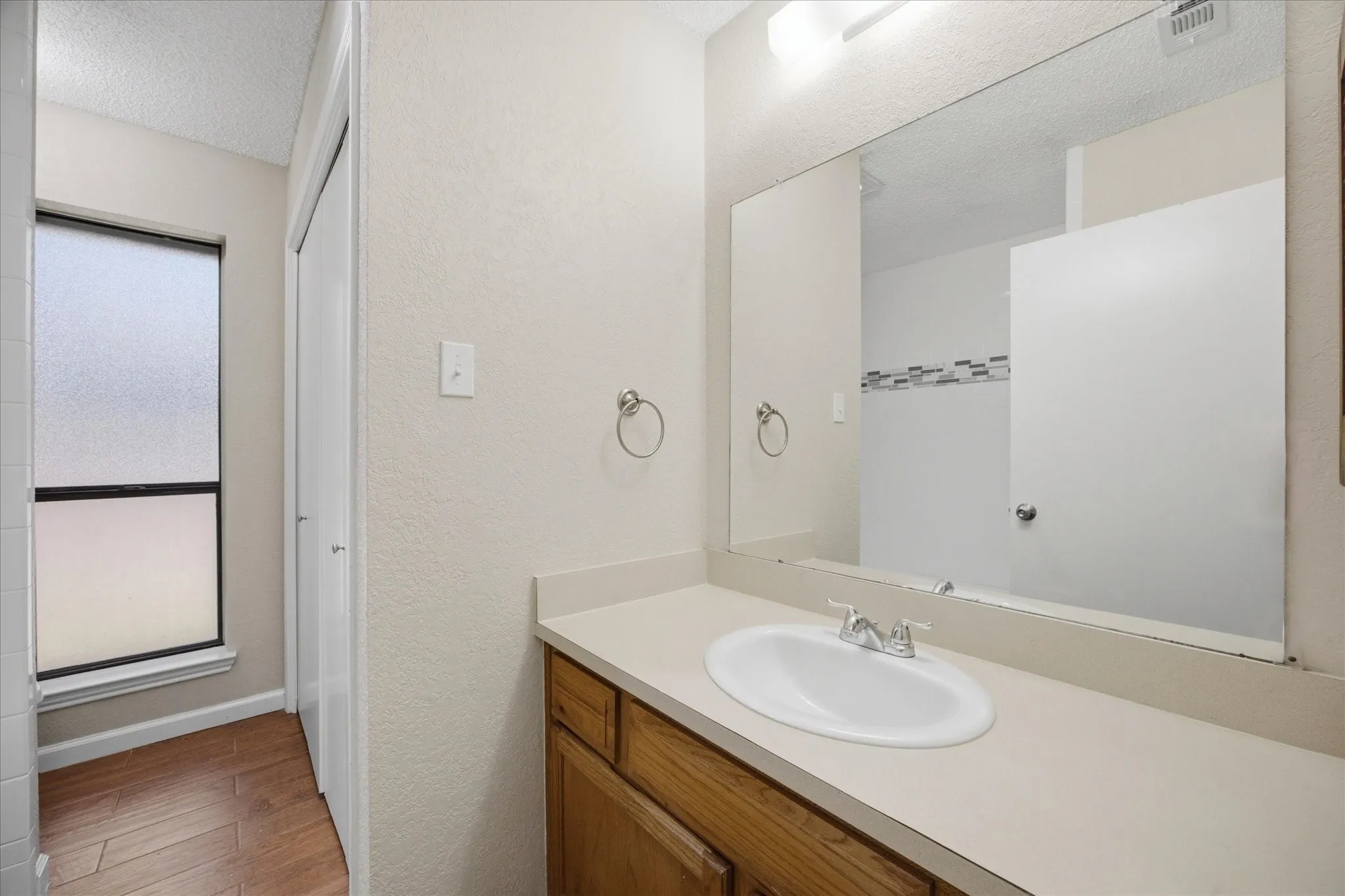 Vanity with integrated sink and chrome faucet, wood-finish cabinetry, and a large wall-mounted mirror