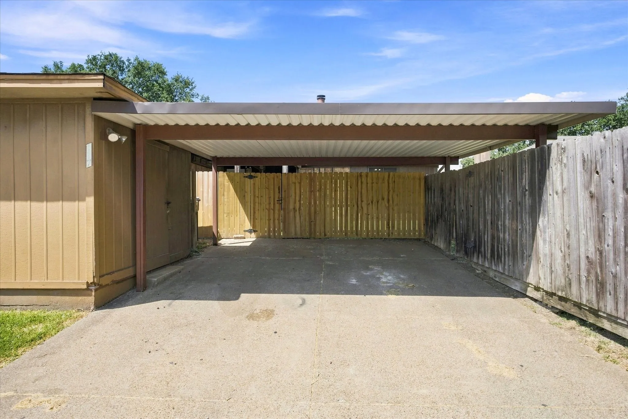 Covered carport with concrete paving, wood-paneled exterior, and a privacy fence