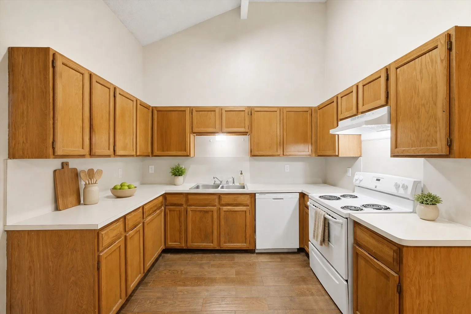 Kitchen featuring abundant wood cabinetry, white countertops, white appliances, a vaulted ceiling, and wood-finish flooring