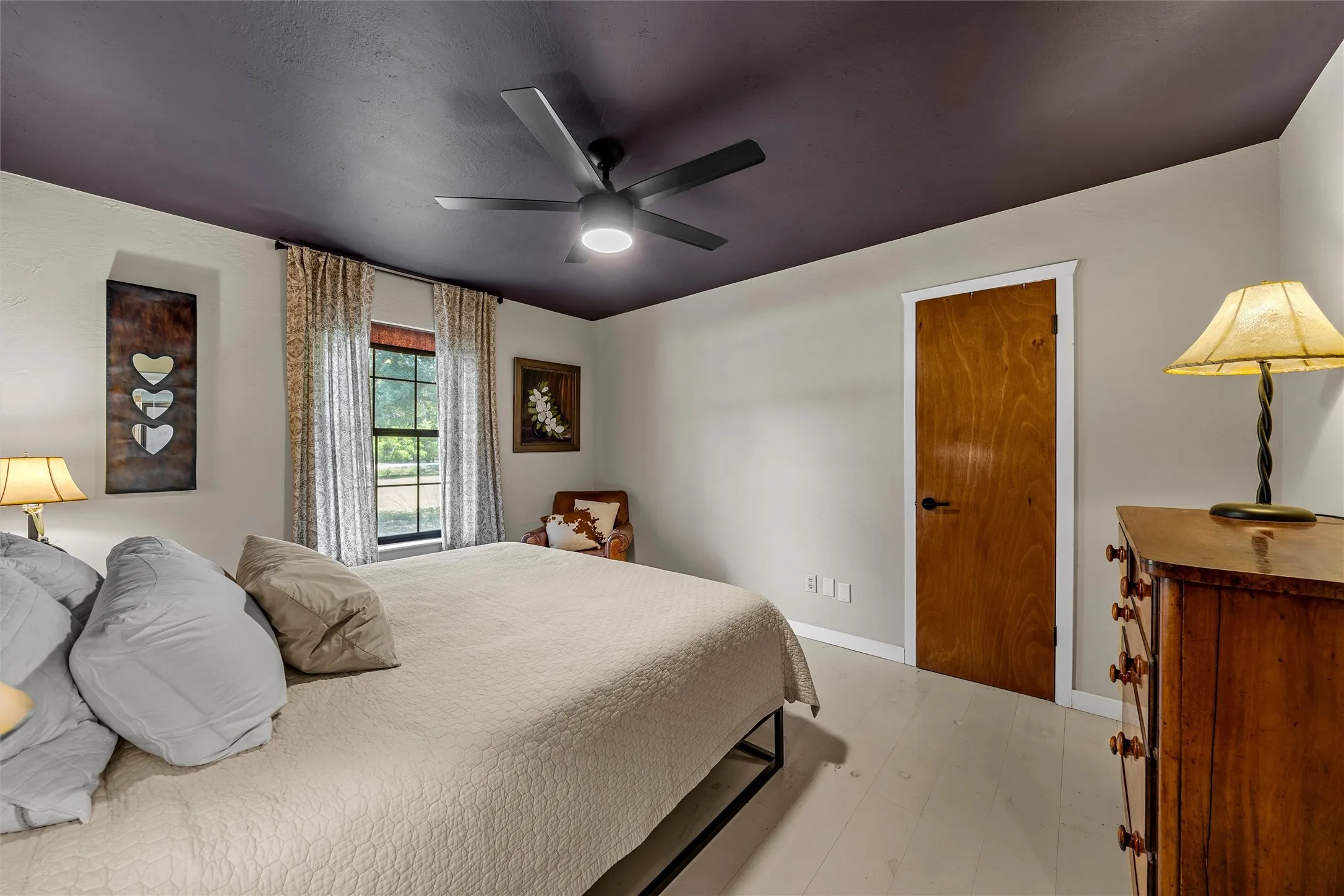 Ceiling fan with integrated lighting, wood-finish door, light-toned flooring, window with drapes, and a contrasting ceiling color