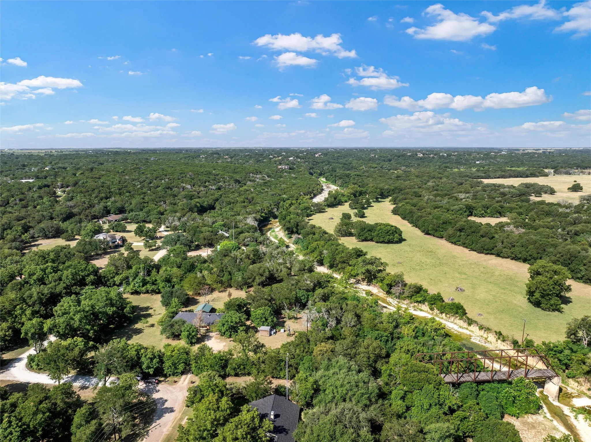 Expansive natural landscape with dense tree coverage, open grassy areas, and a visible bridge structure