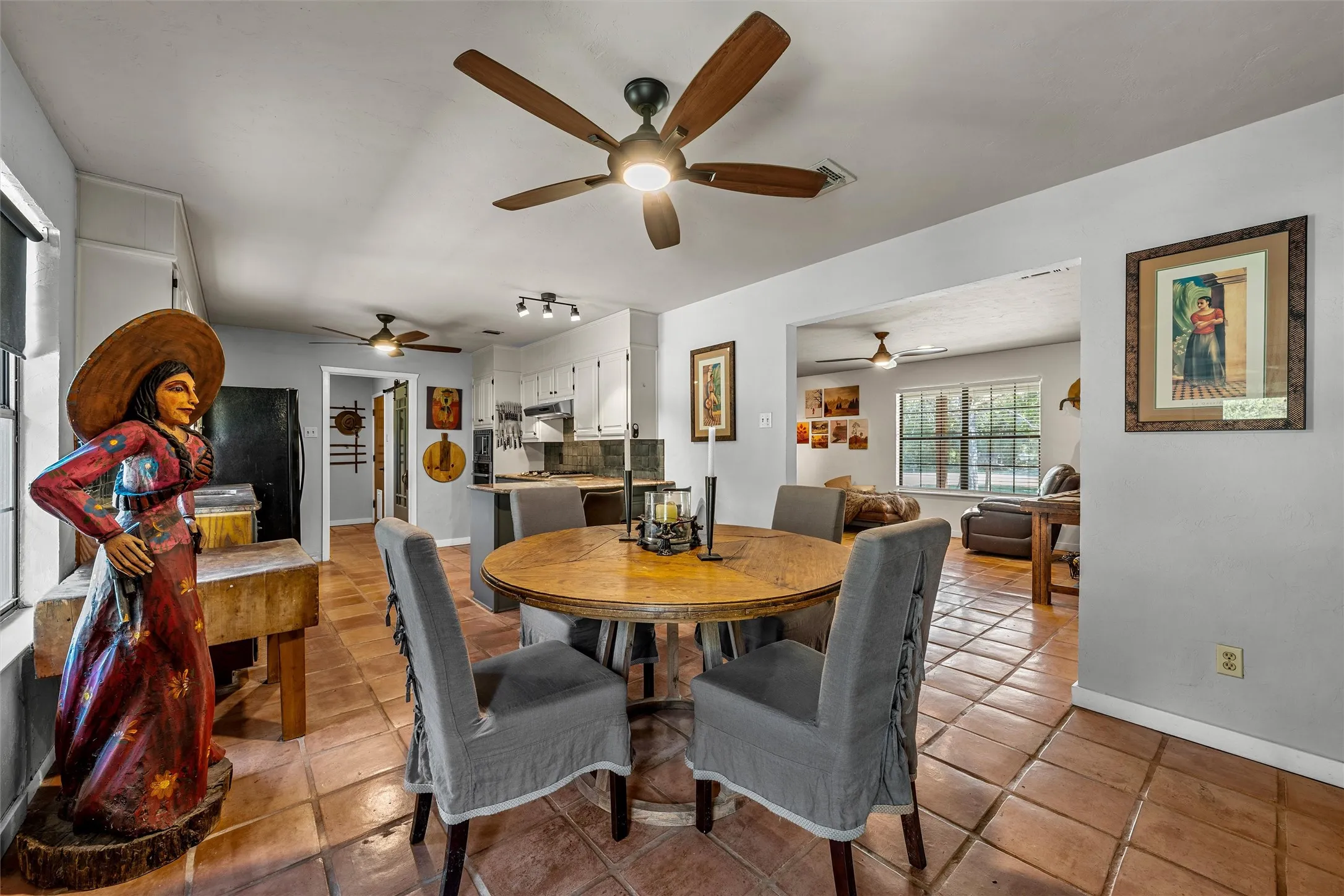 Terracotta tile flooring throughout, ceiling fans with integrated lighting, kitchen area with white cabinetry, and recessed lighting
