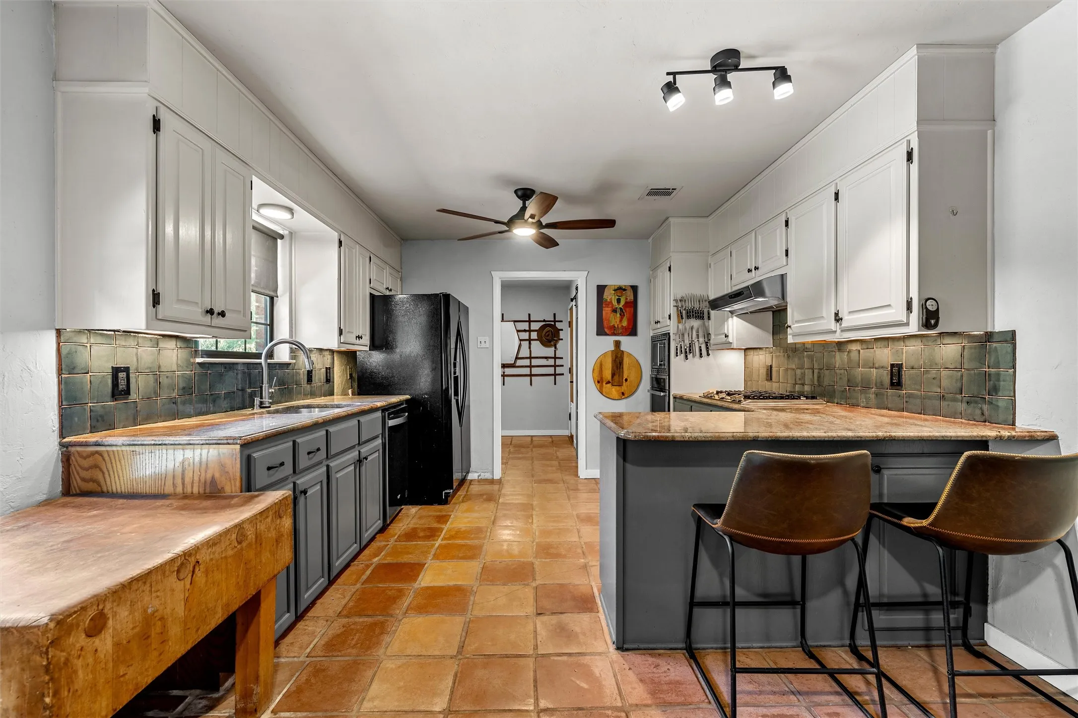 Kitchen with terracotta tile flooring, white upper cabinetry, dark gray lower cabinetry, a built-in butcher block counter, and a built-in breakfast bar