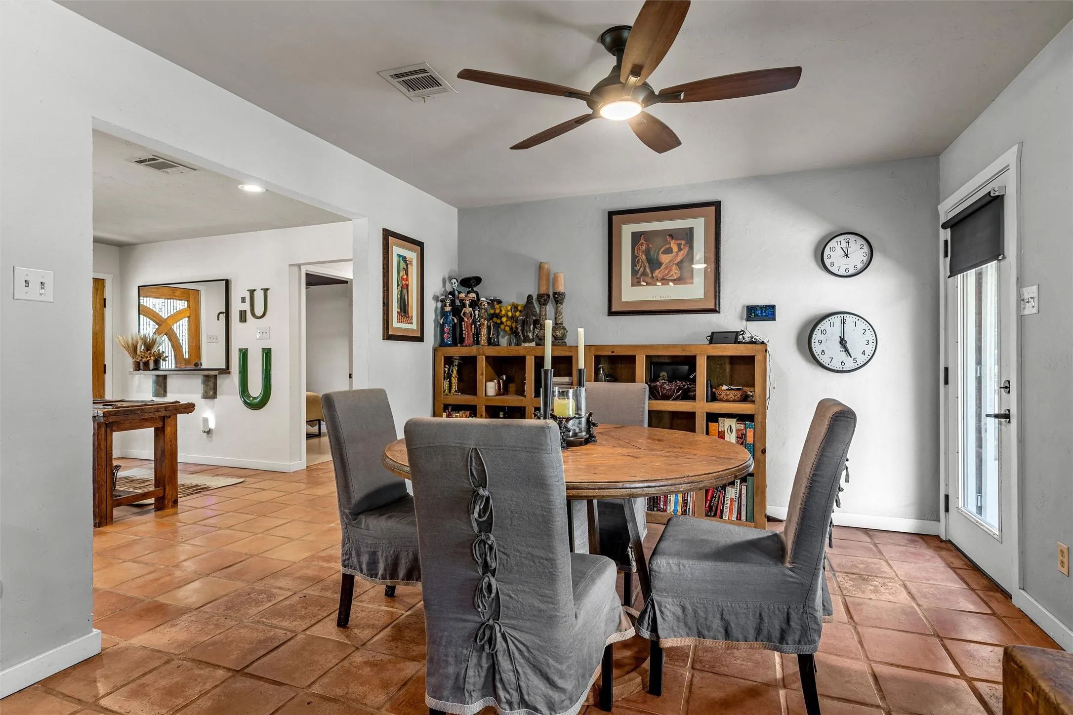 Terra cotta tile flooring, wood-finish ceiling fan with integrated lighting, built-in wooden shelving, and a glass-paneled door