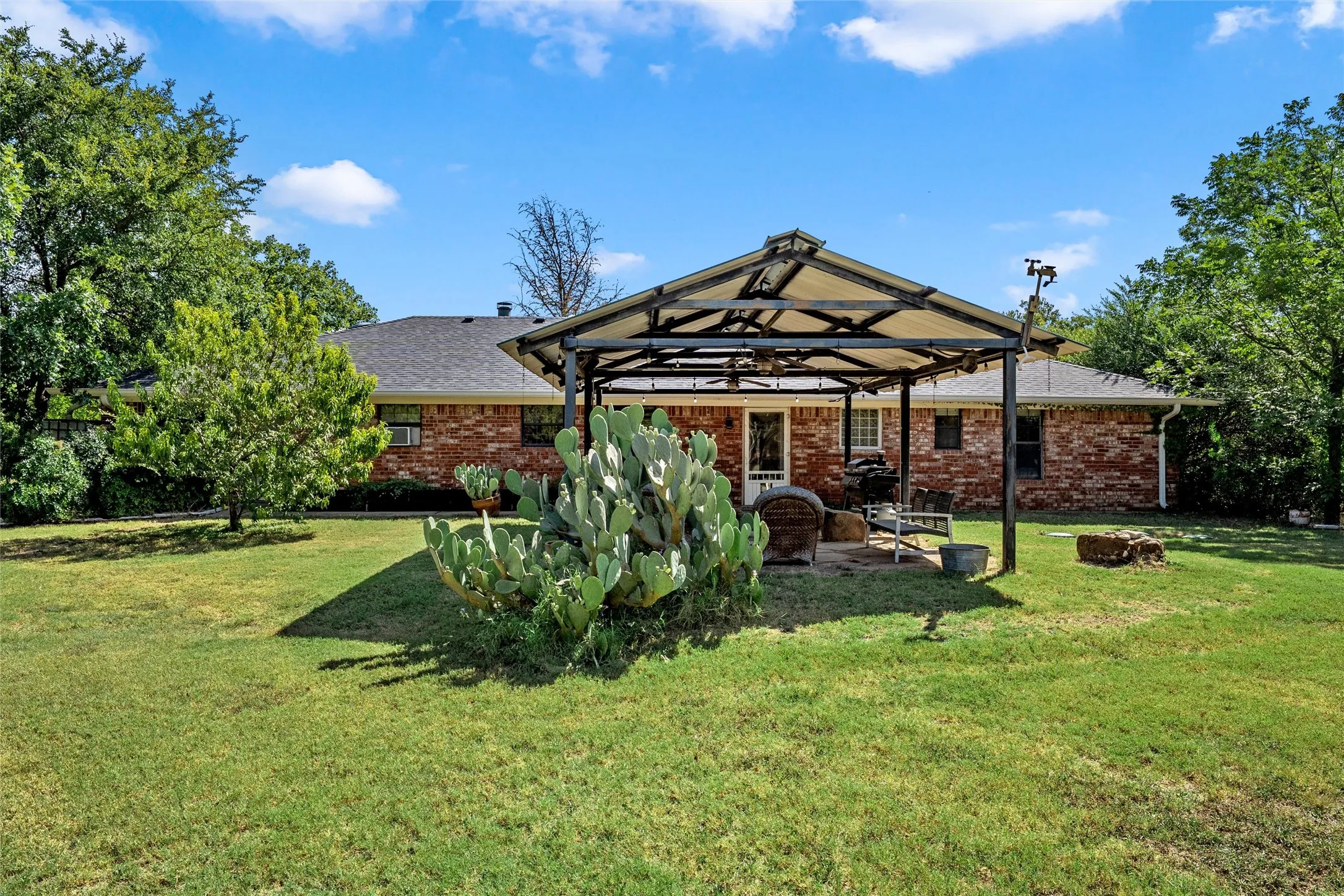 Expansive backyard featuring a brick exterior, covered patio structure, and lush landscaping