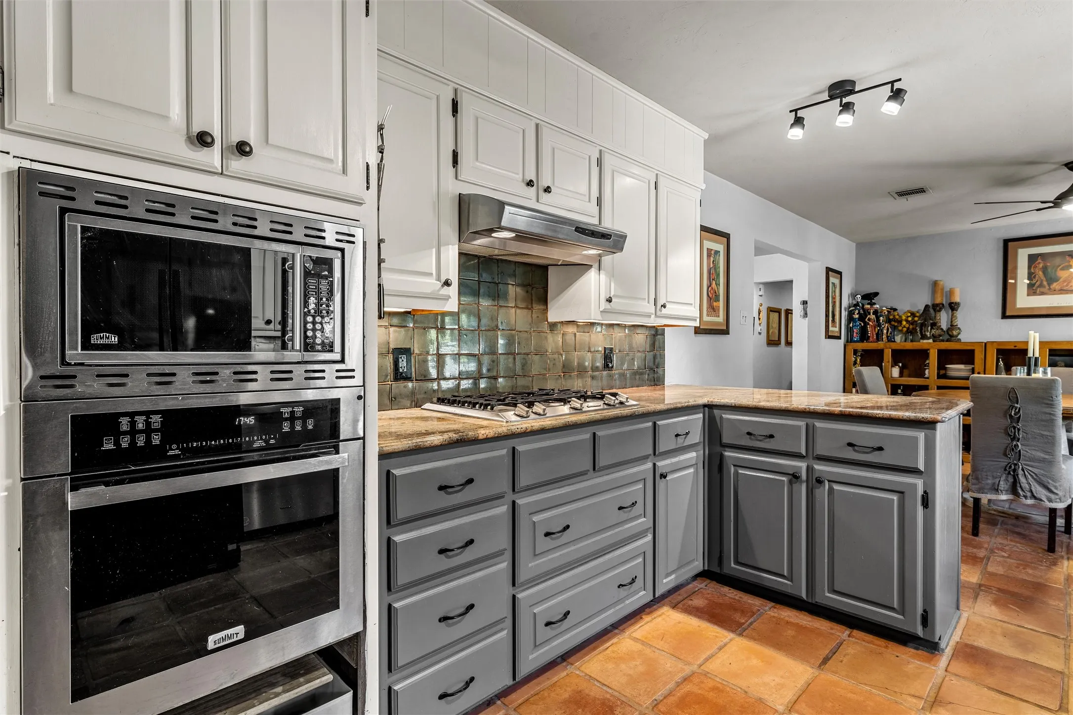 Stainless steel built-in microwave and oven, gas cooktop, tile backsplash, granite countertops, and terracotta tile flooring