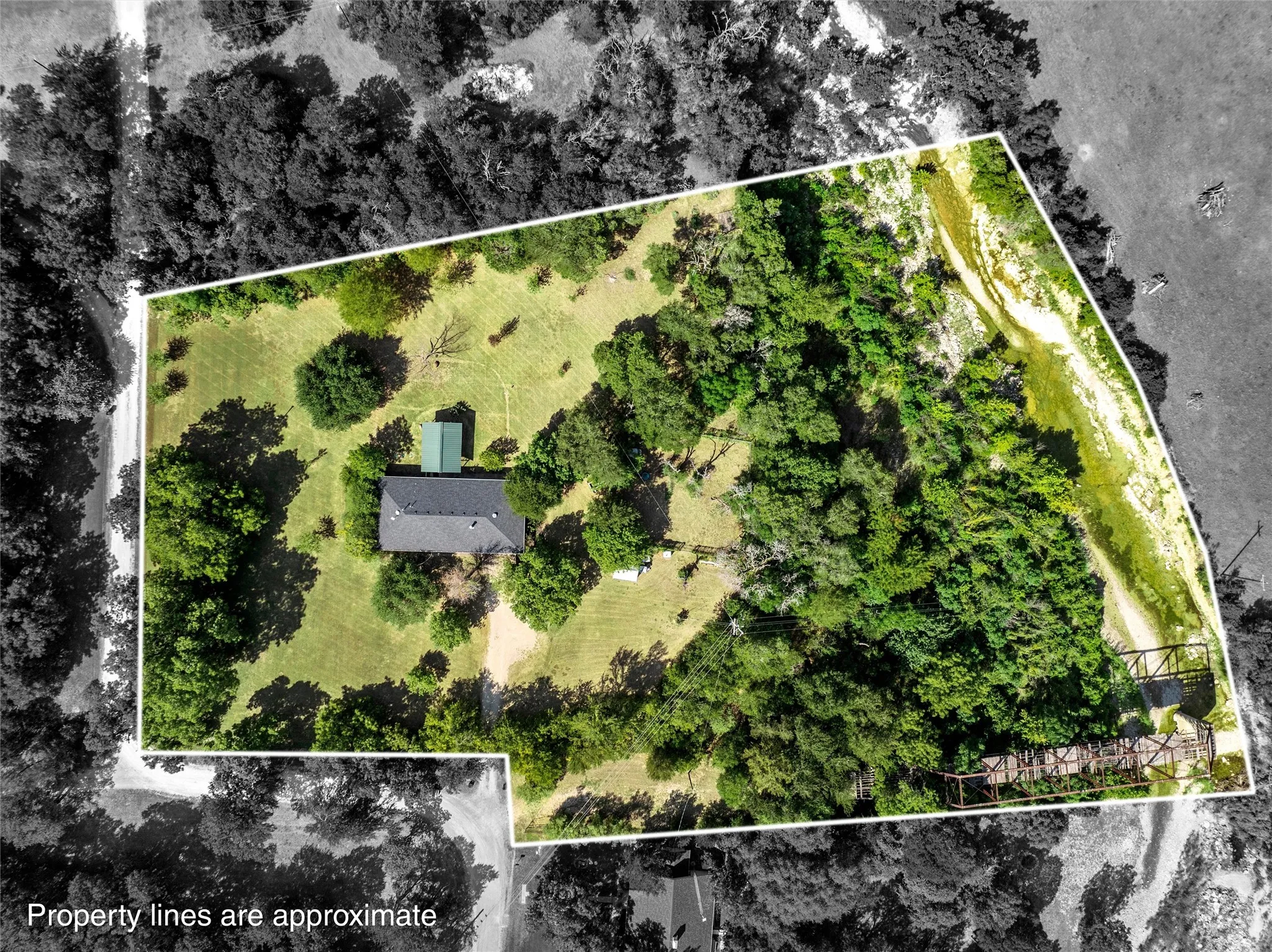Expansive property featuring a single-story residence with a dark roof, a separate green outbuilding, mature trees, and a natural watercourse bordering one side