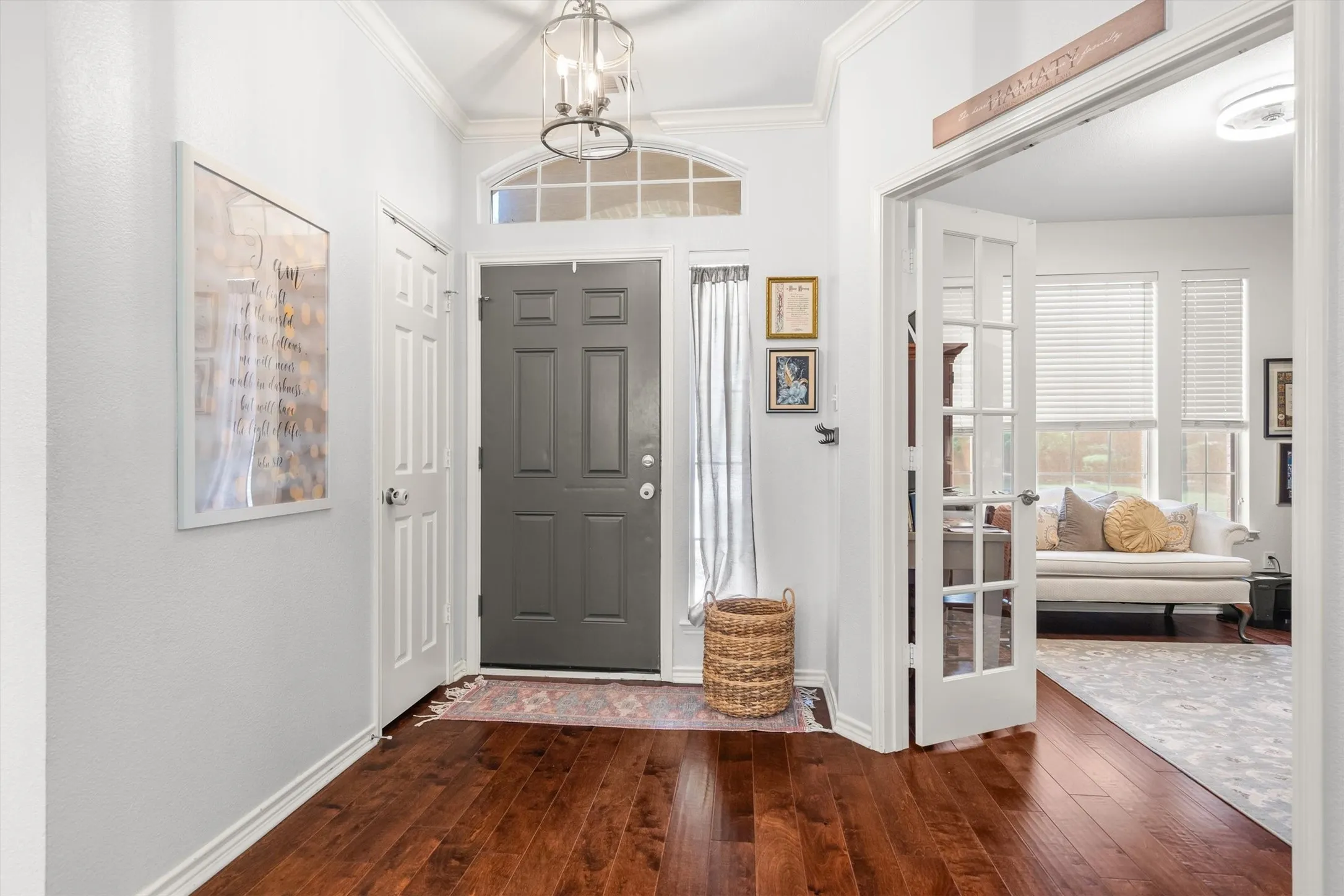 Hardwood-finish flooring, a paneled entry door with sidelights and transom window, a semi-flush mount ceiling light, crown molding, and French doors