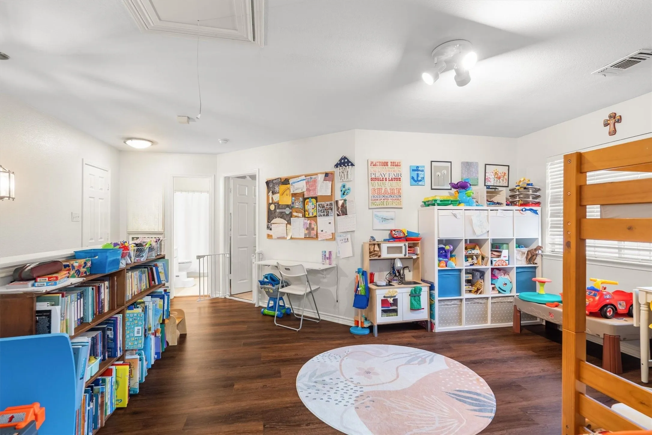 Spacious room featuring wood-finish flooring, white walls, and a track lighting fixture
