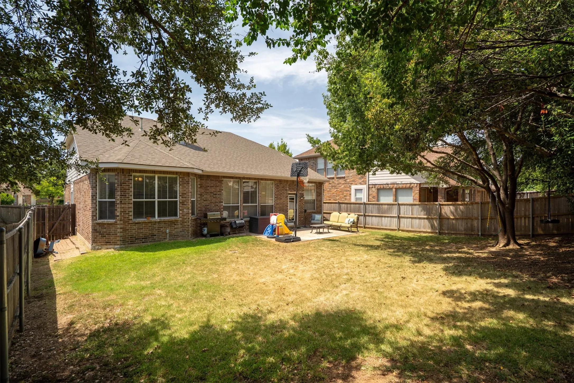 Expansive backyard featuring a brick exterior, shingle roof, multiple windows, and a wooden privacy fence