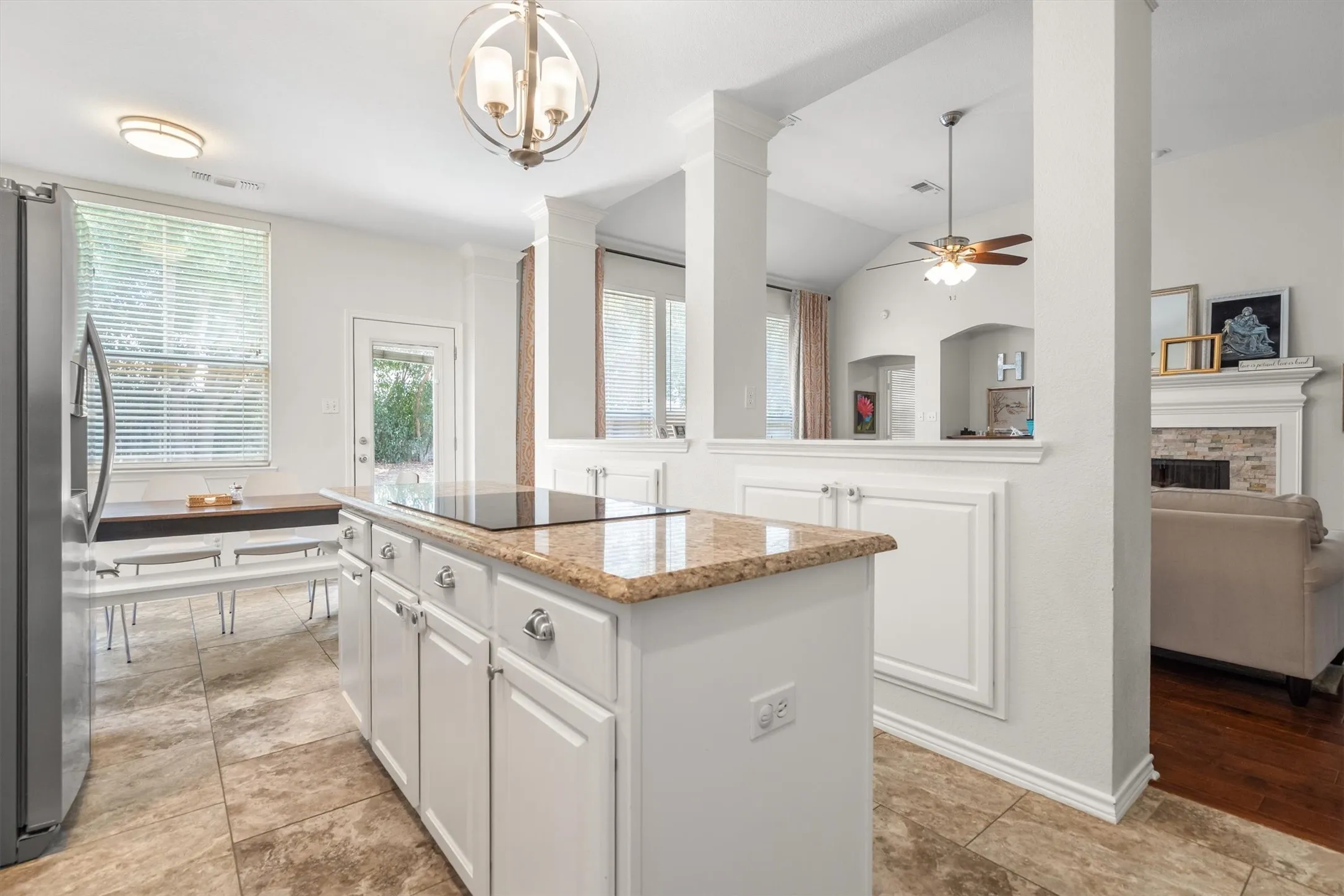 Kitchen island with a built-in cooktop, granite countertop, and white cabinetry