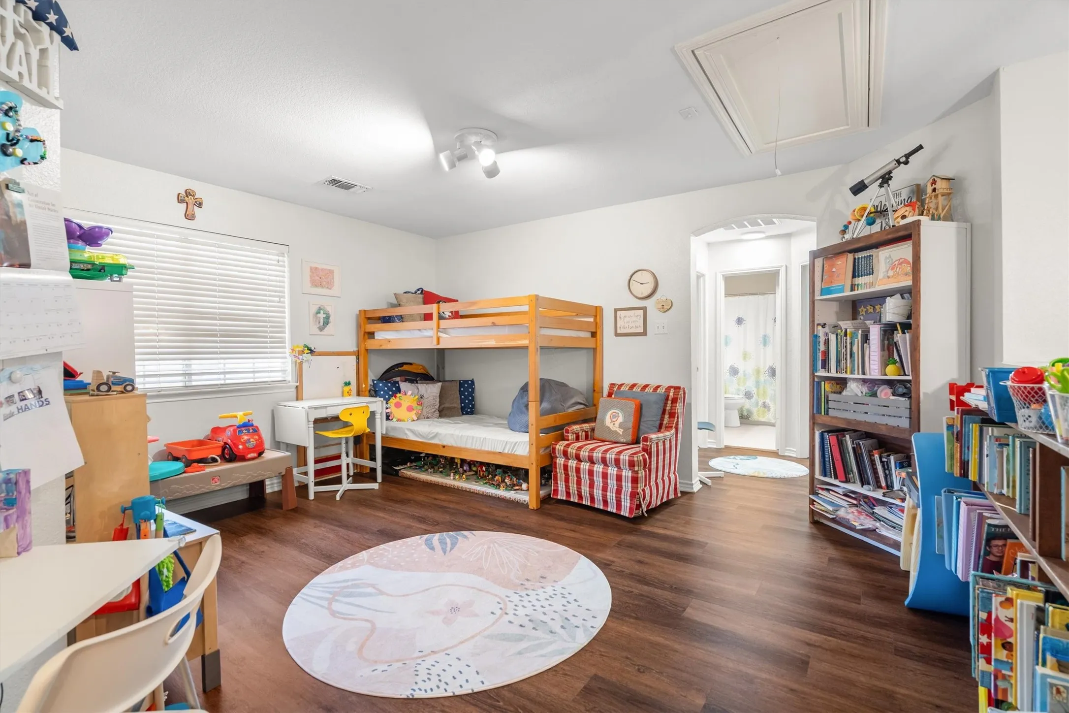 Room featuring wood-finish flooring, white walls, a recessed window with blinds, and an arched doorway