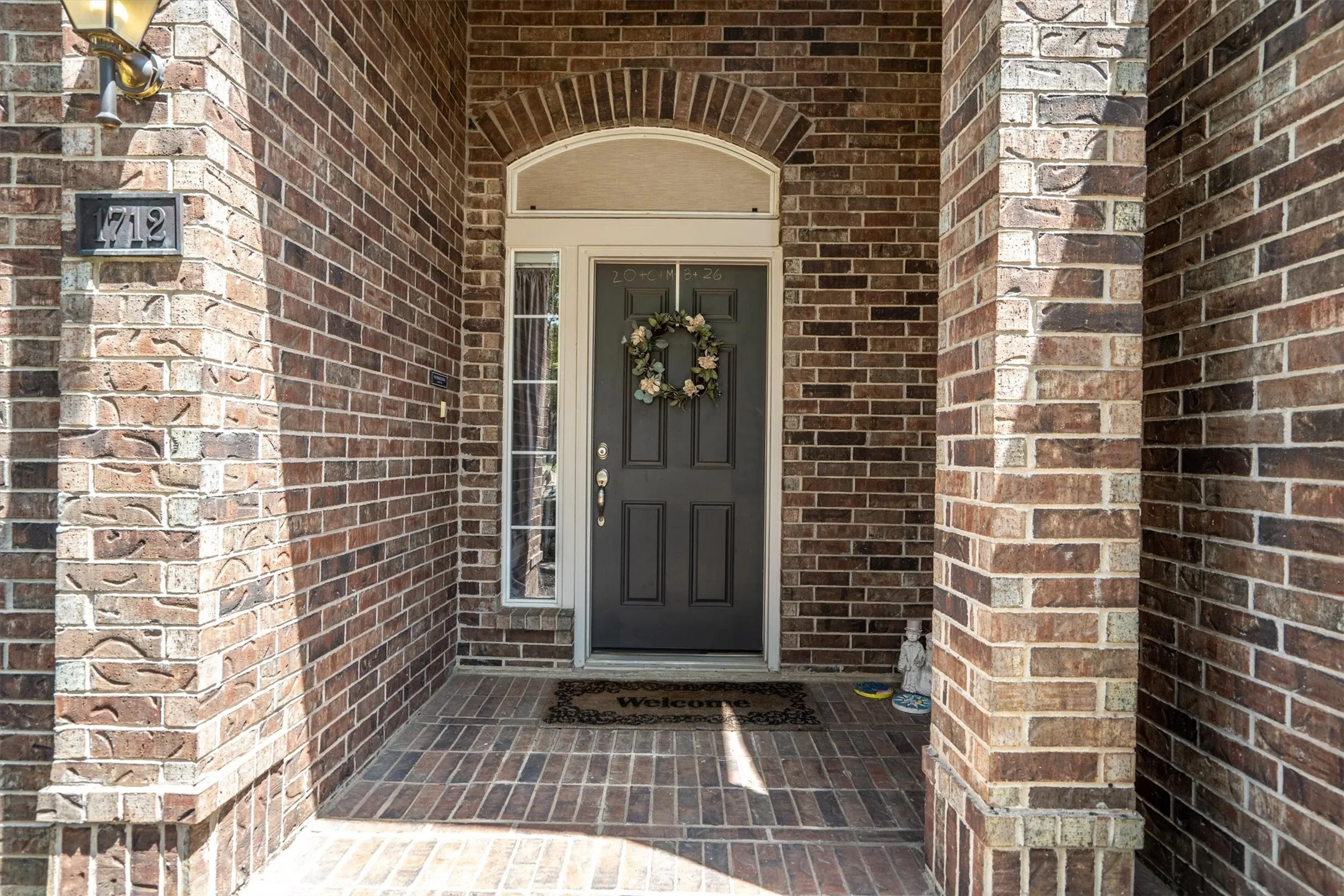 Brick exterior with an arched entryway, transom window, sidelight, and brick paver porch