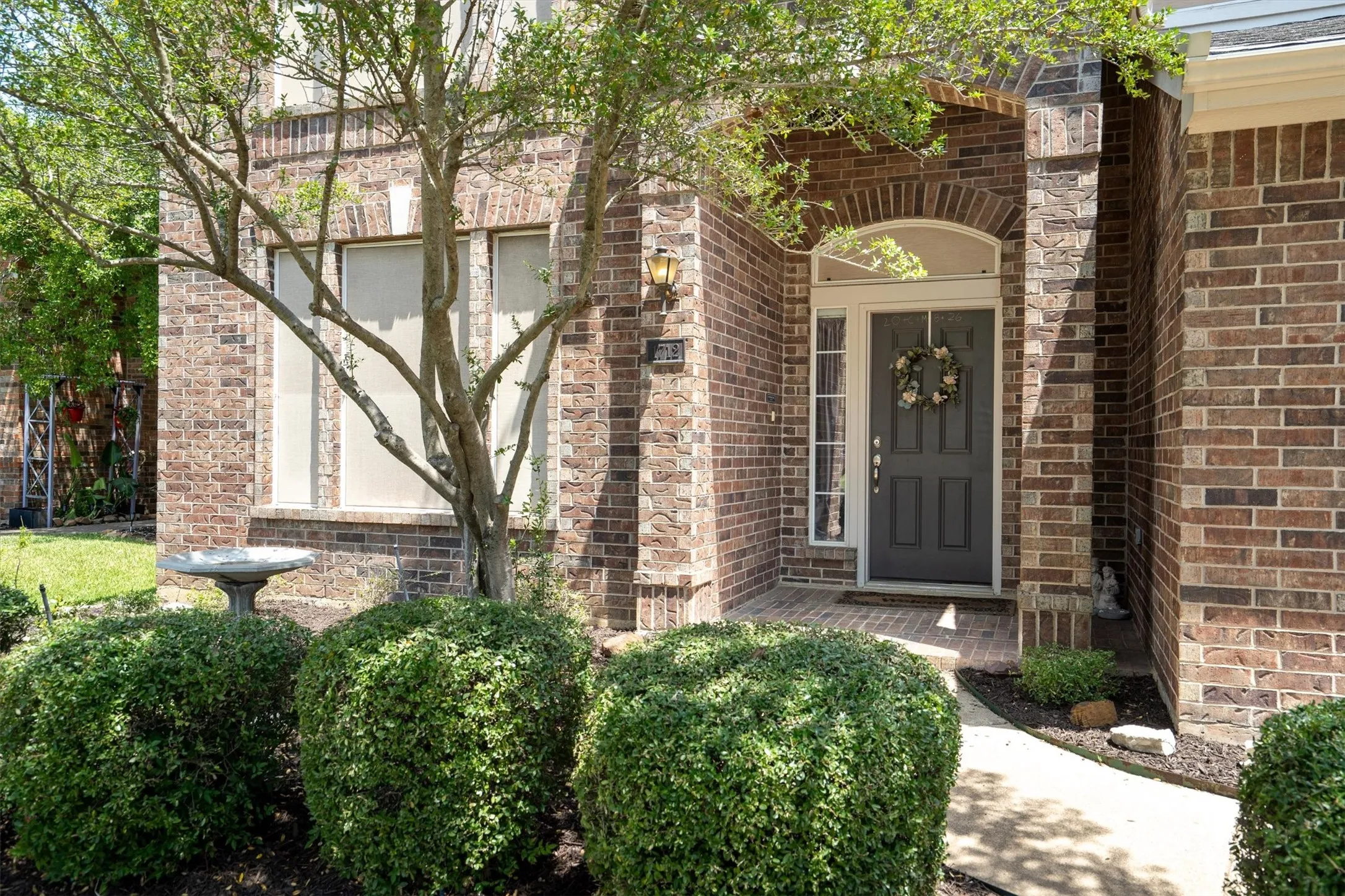 Brick exterior featuring an arched entryway, transom window, and mature landscaping with manicured shrubs