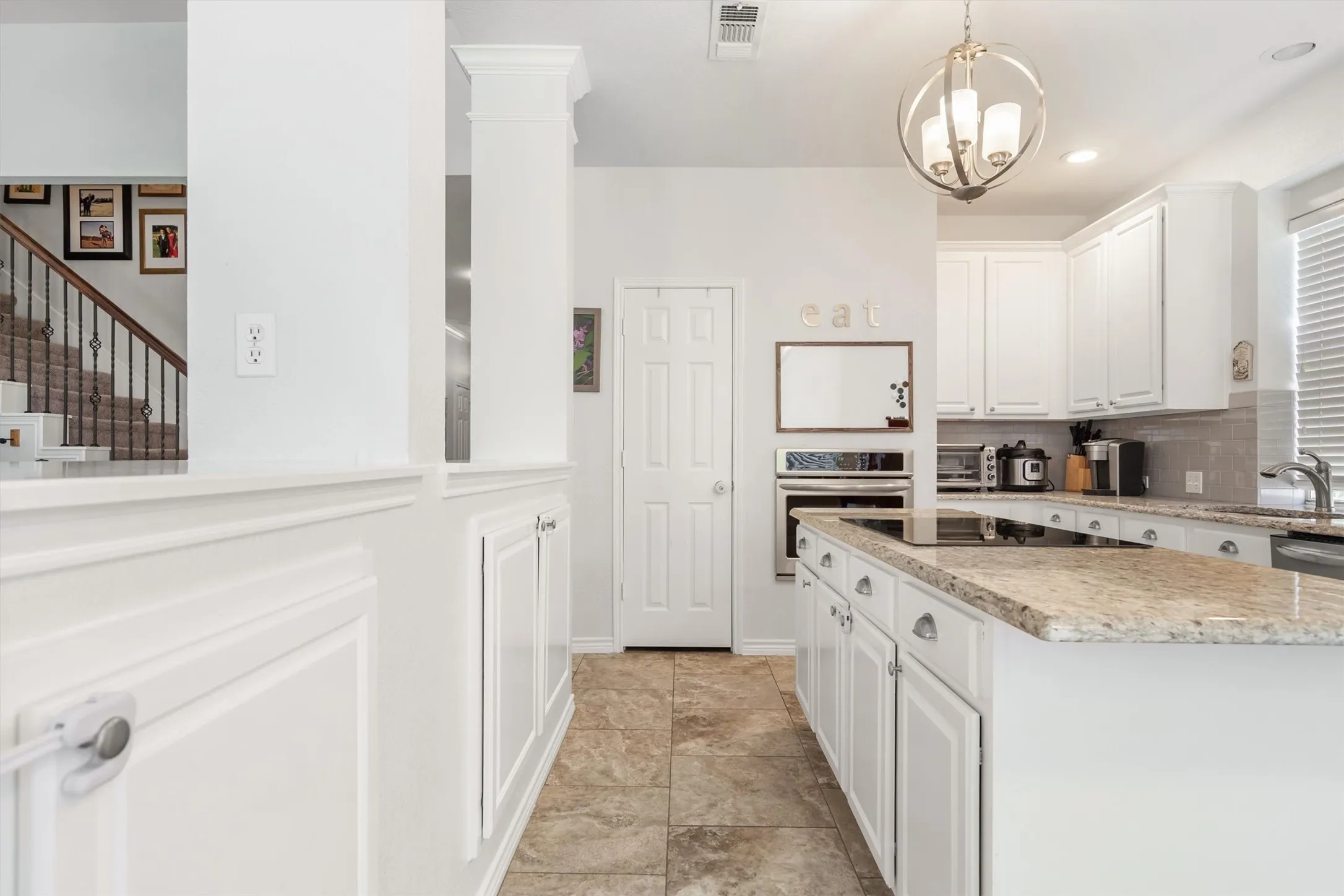 Kitchen featuring an island with a built-in cooktop, light-toned countertops, white cabinetry, and a built-in oven