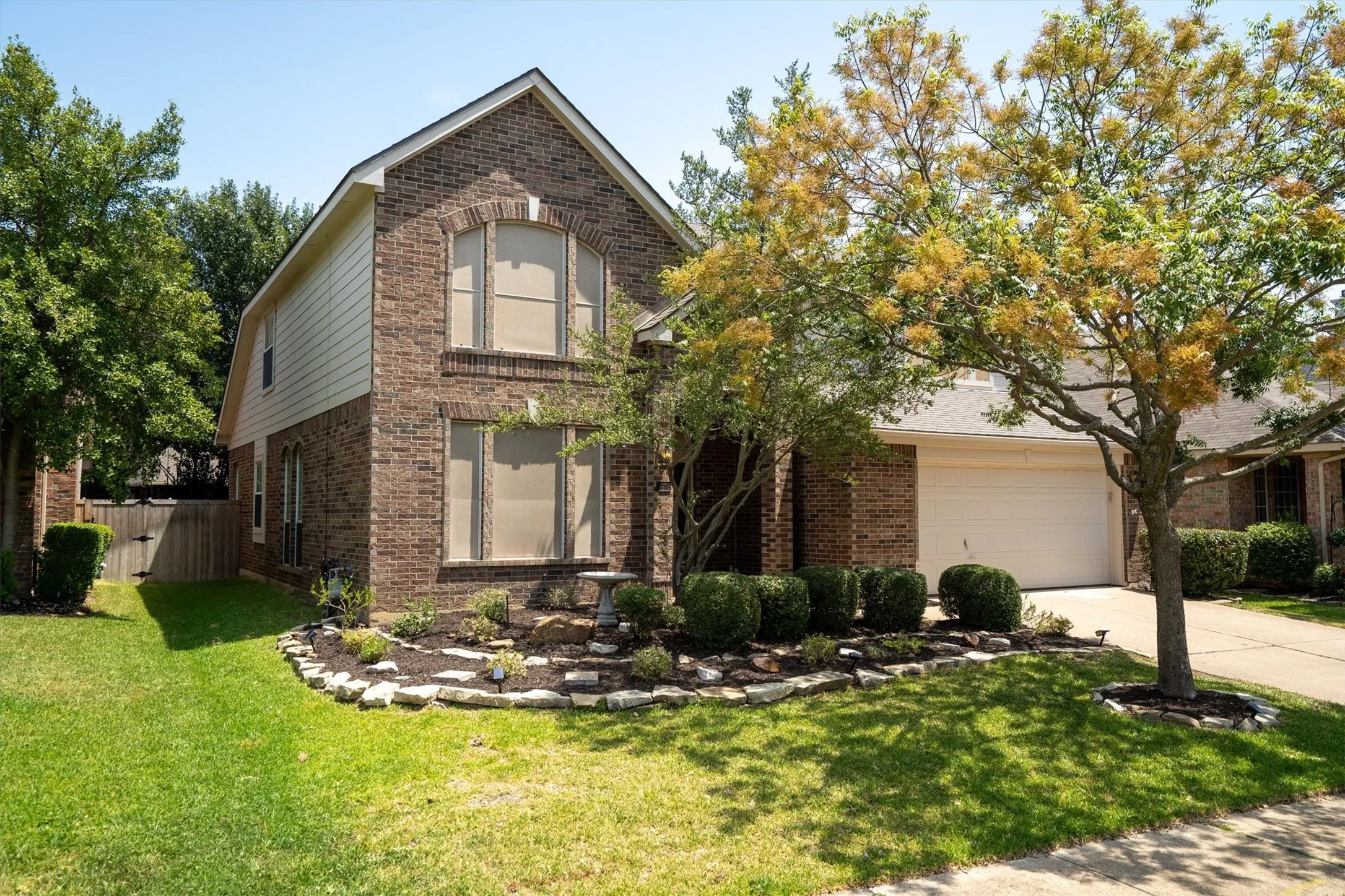 Brick facade, arched windows, attached two-car garage, established front yard landscaping, and mature trees