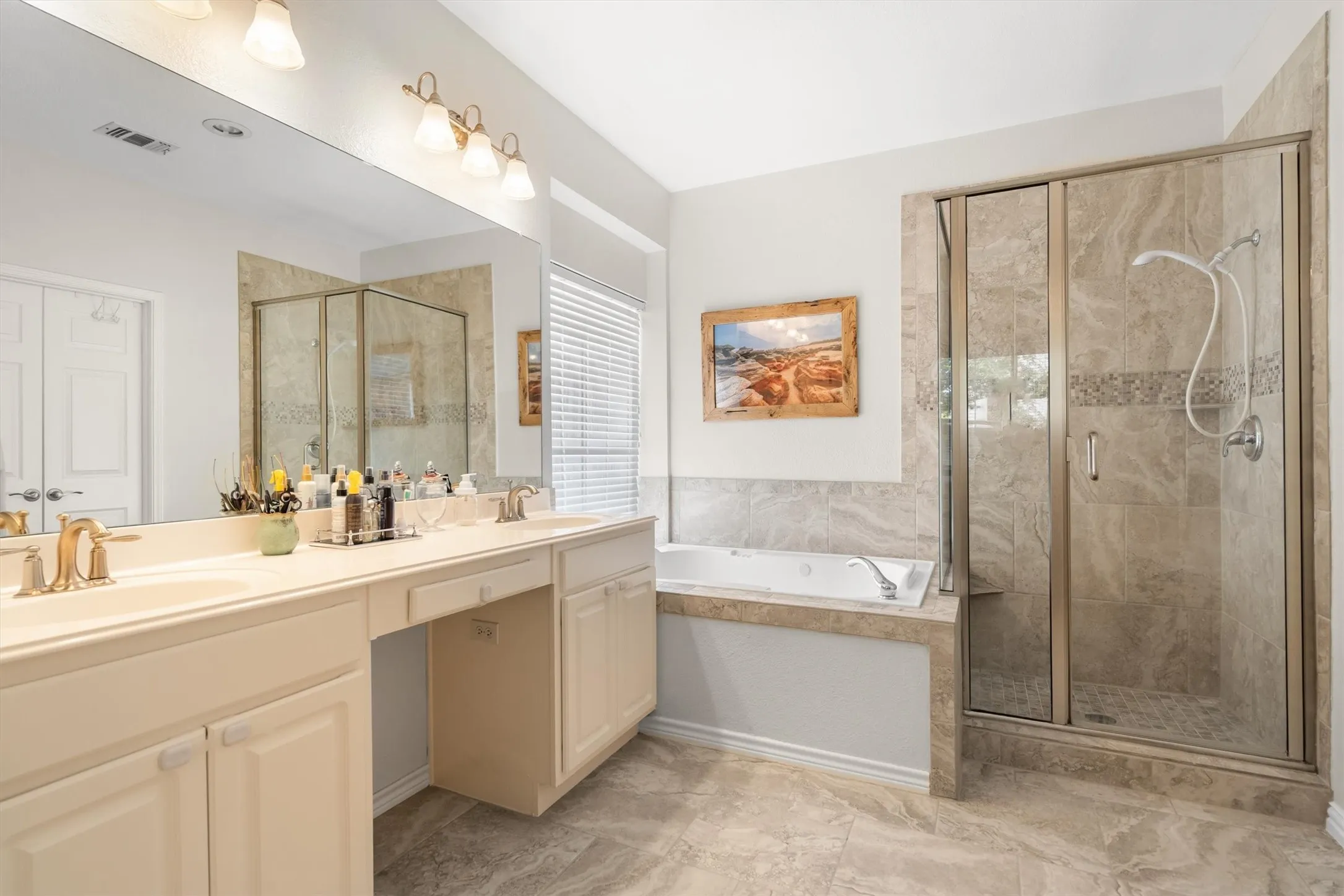 Spacious bathroom featuring dual vanity with integrated sinks, built-in cabinetry, a soaking tub, and a glass-enclosed shower