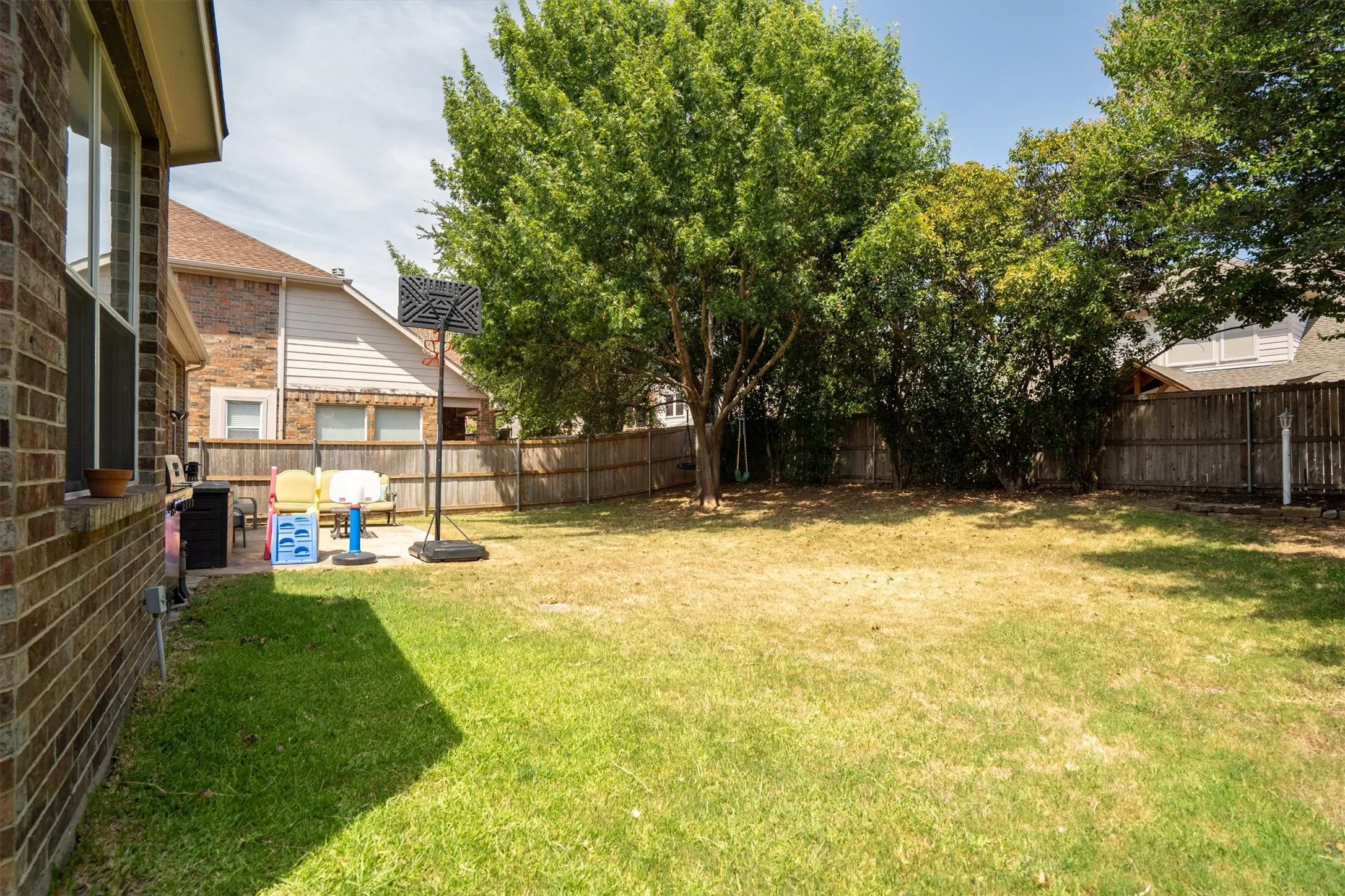 Expansive grass yard with mature trees, a wooden privacy fence, and a brick exterior