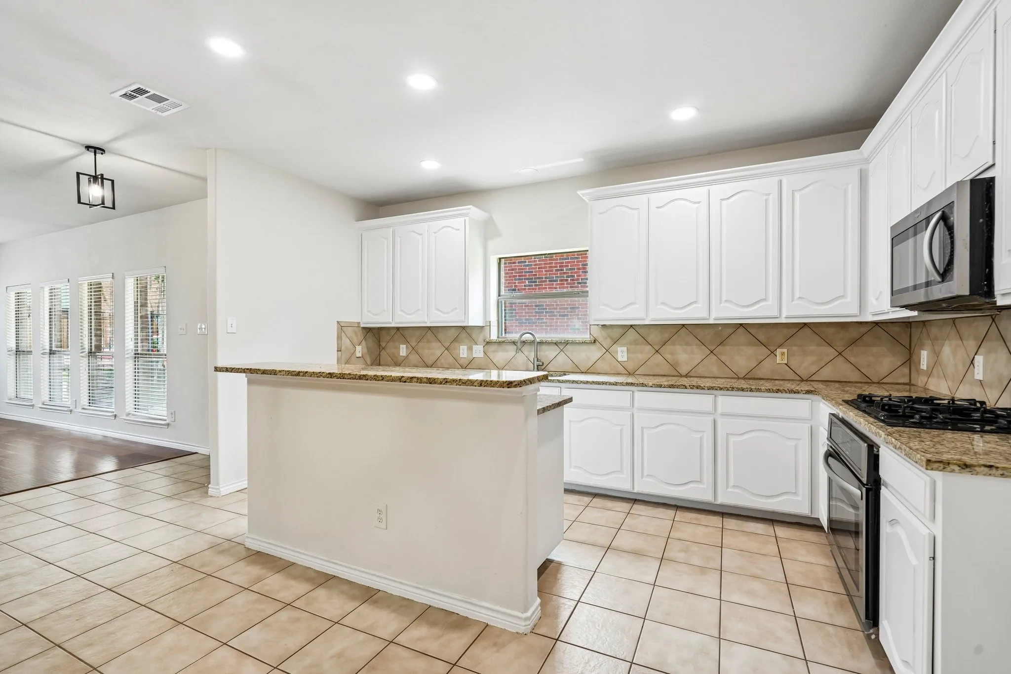 Bright, spacious kitchen featuring crisp white cabinetry, granite countertops with kitchen island.