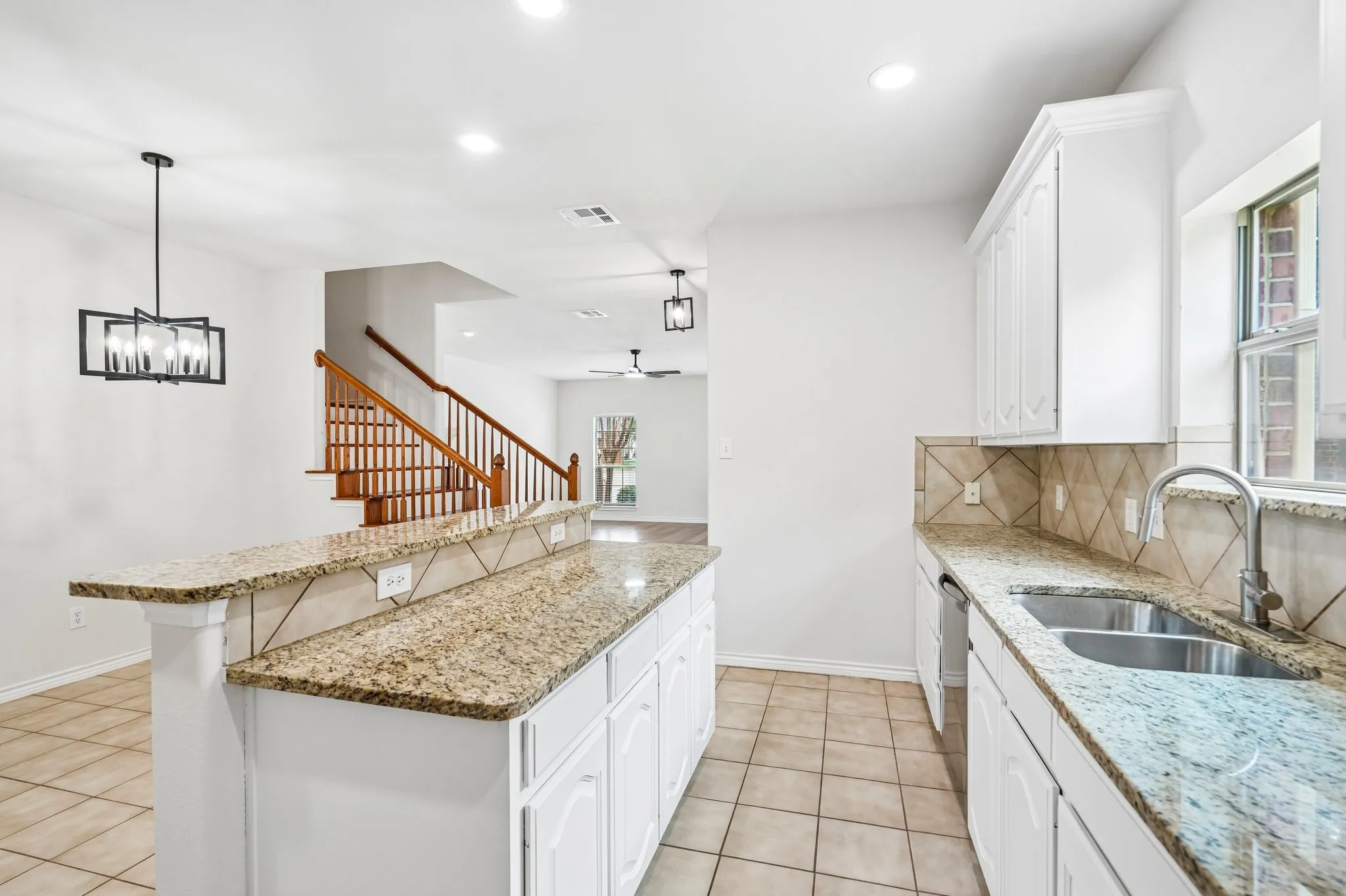 Bright, spacious kitchen featuring crisp white cabinetry, granite countertops, stainless-steel appliances, ample storage, and a stylish modern light fixture