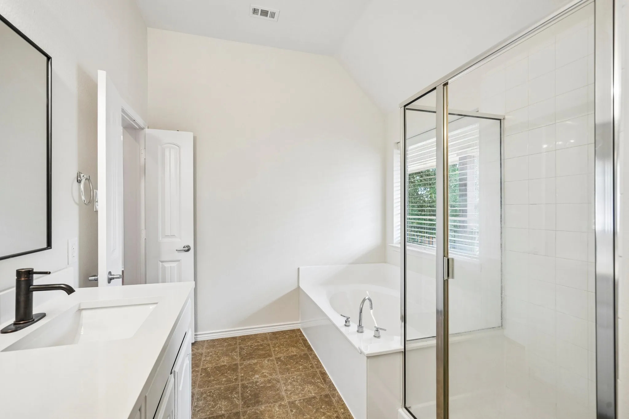 Spacious primary bathroom featuring a soaking tub, separate glass-enclosed shower, dual-sink vanity, and abundant natural light