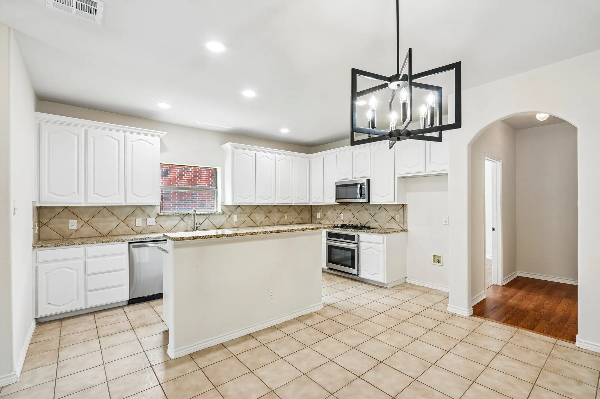 Bright, spacious kitchen featuring crisp white cabinetry, granite countertops, stainless-steel appliances, ample storage, and a stylish modern light fixture