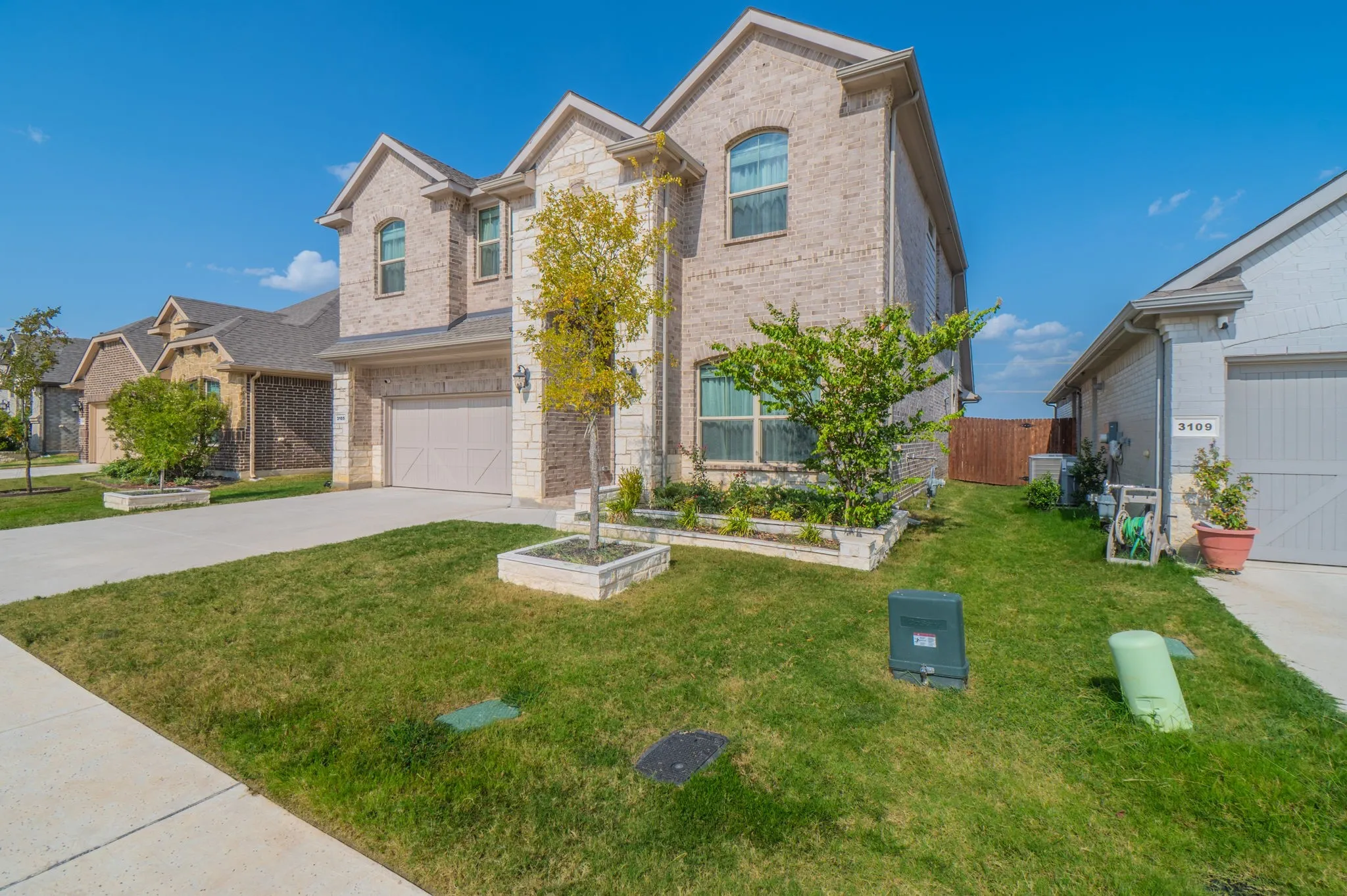 Stone and brick exterior with arched windows, attached garage, concrete driveway, and established landscaping