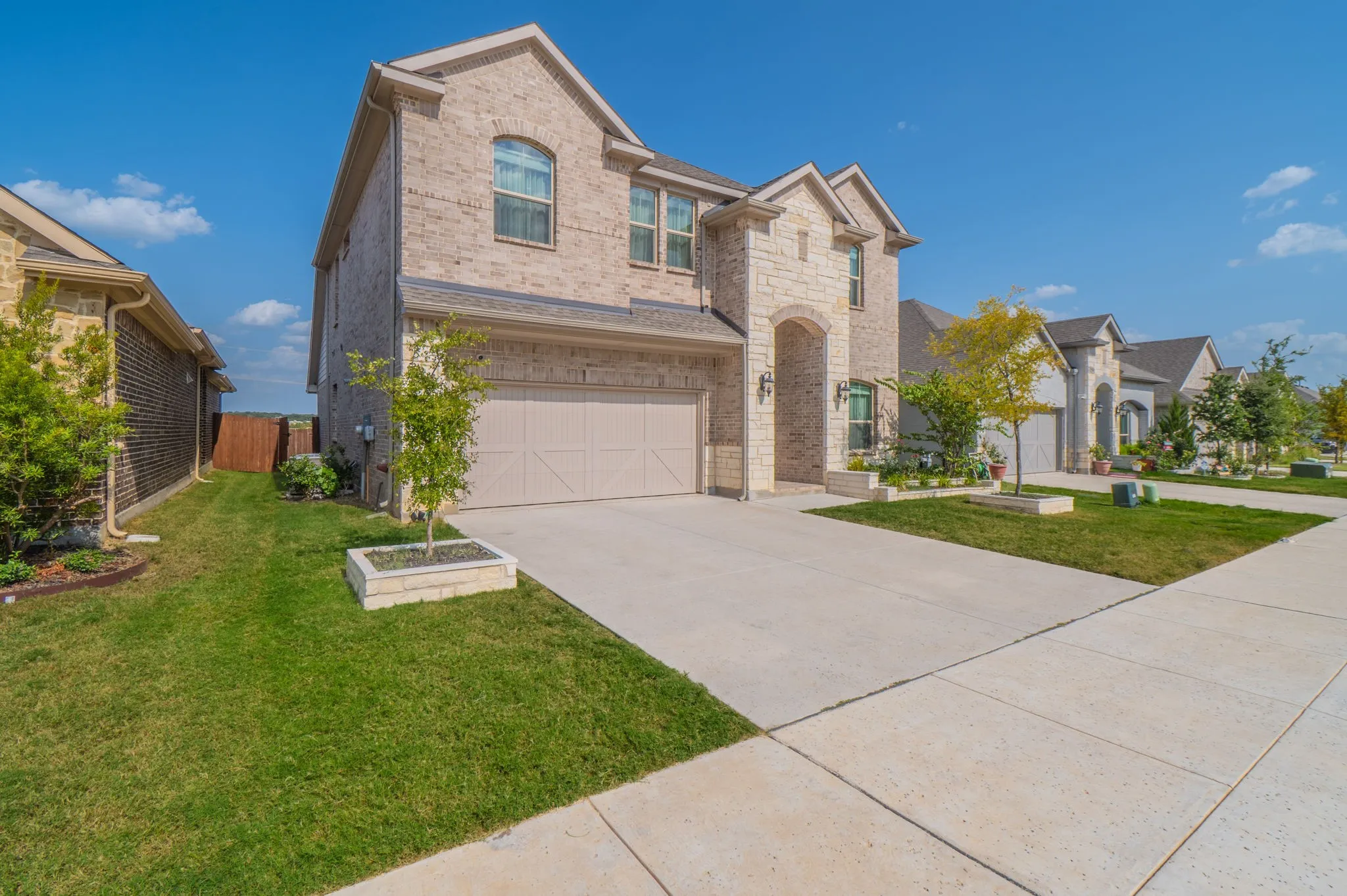 Stone and brick facade with arched entryway, attached two-car garage, and concrete driveway