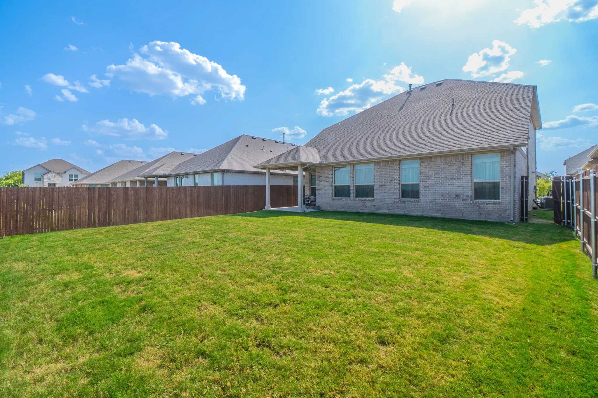Expansive grassy yard with a privacy fence, covered patio, and brick exterior