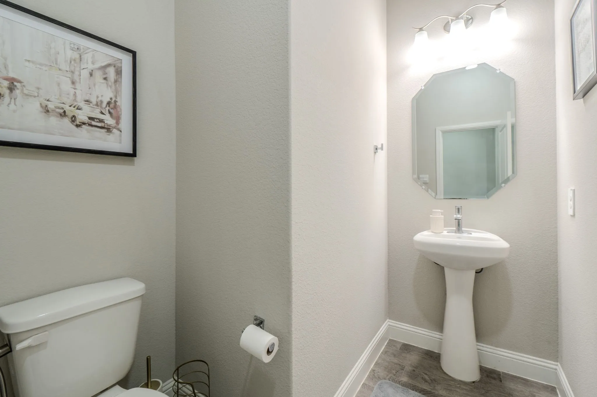 Pedestal sink with a polished chrome faucet, octagonal mirror, and a three-light vanity fixture
