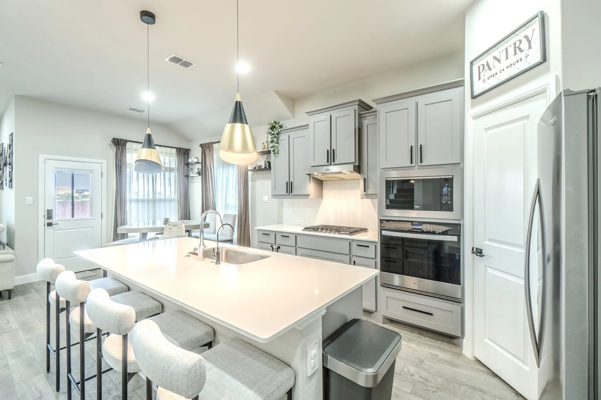 Kitchen featuring a large island with an undermount sink, light gray cabinetry, stainless steel appliances, and wood-finish flooring