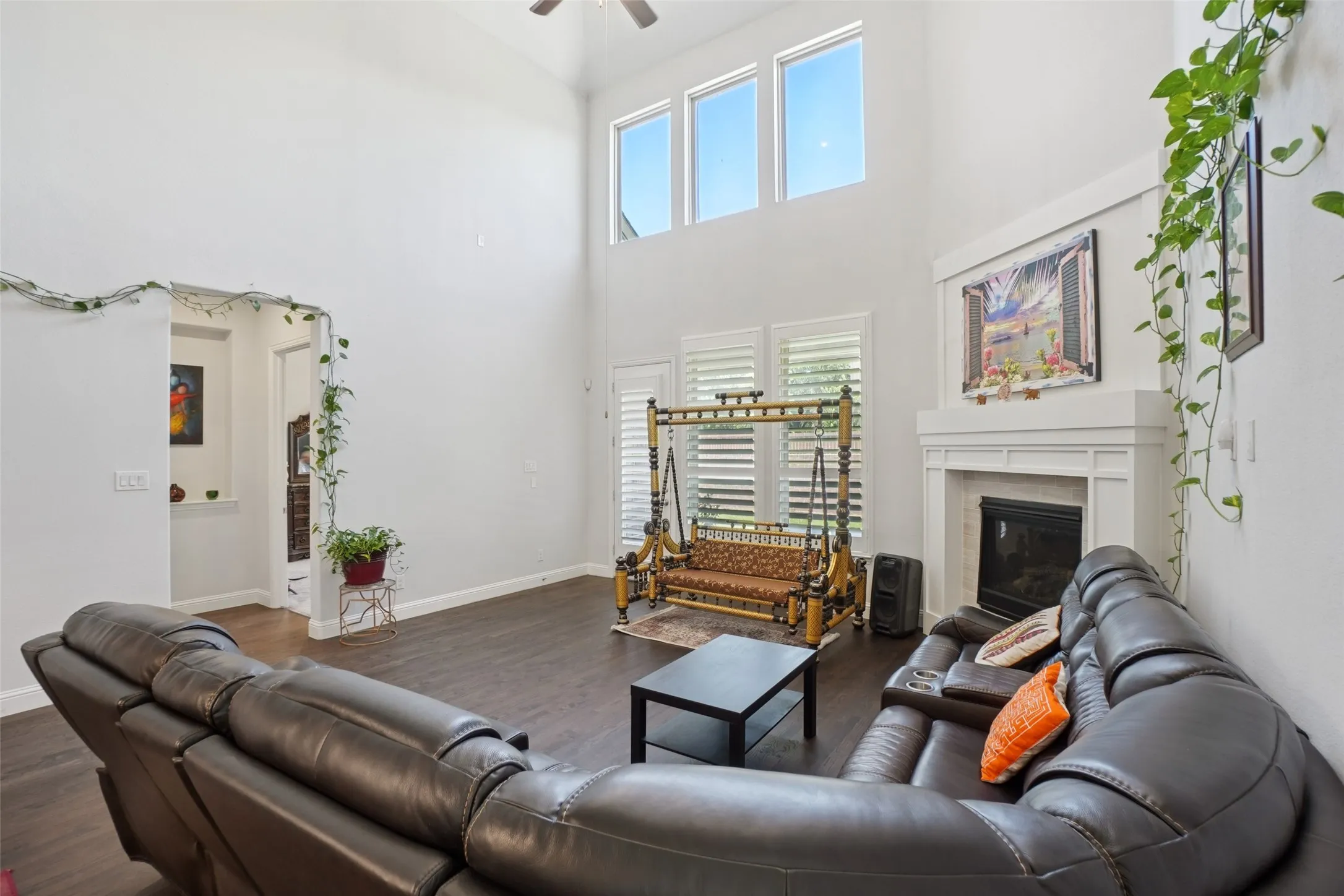 Living room with a towering ceiling, wood finished floors, a ceiling fan, and a glass covered fireplace