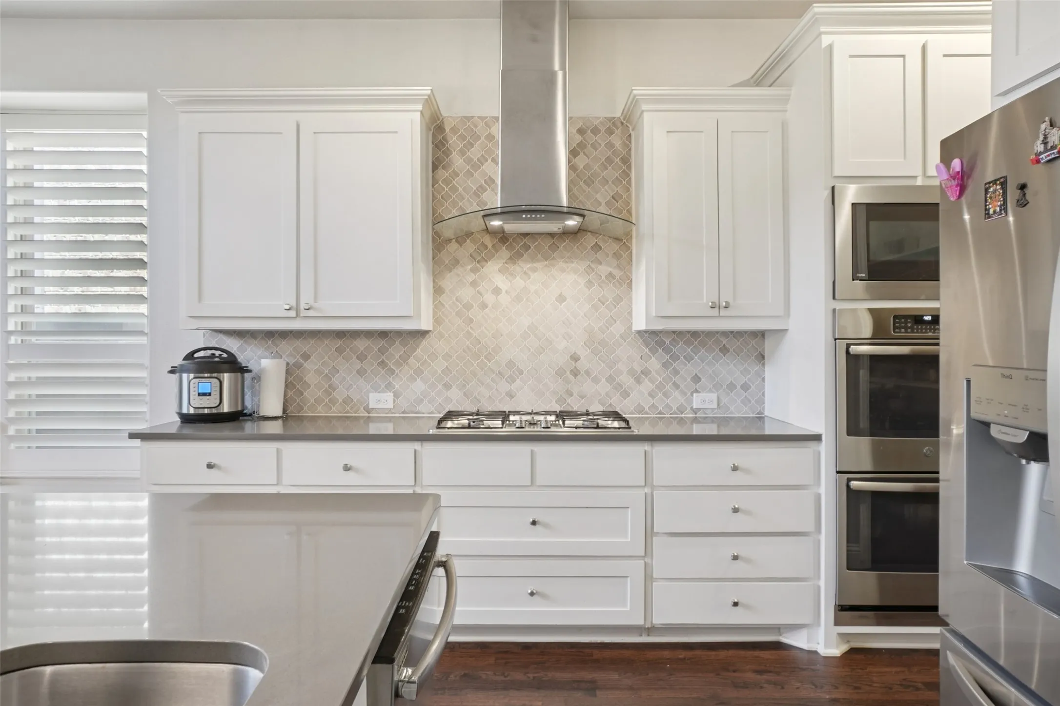 Kitchen featuring appliances with stainless steel finishes, wall chimney exhaust hood, decorative backsplash, and white cabinets