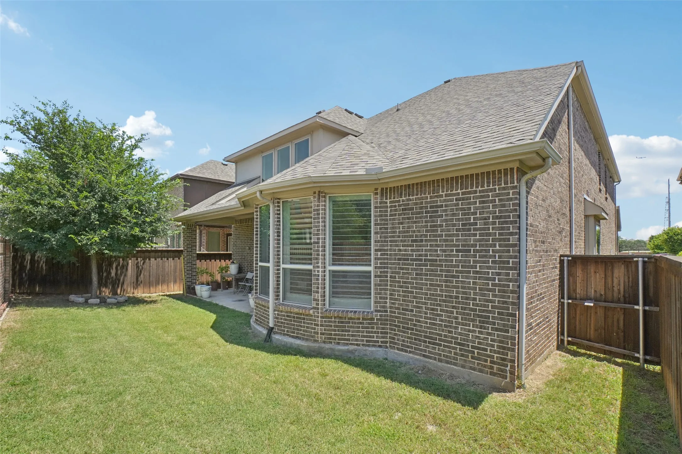 Rear view of house featuring brick siding, a fenced backyard, and roof with shingles