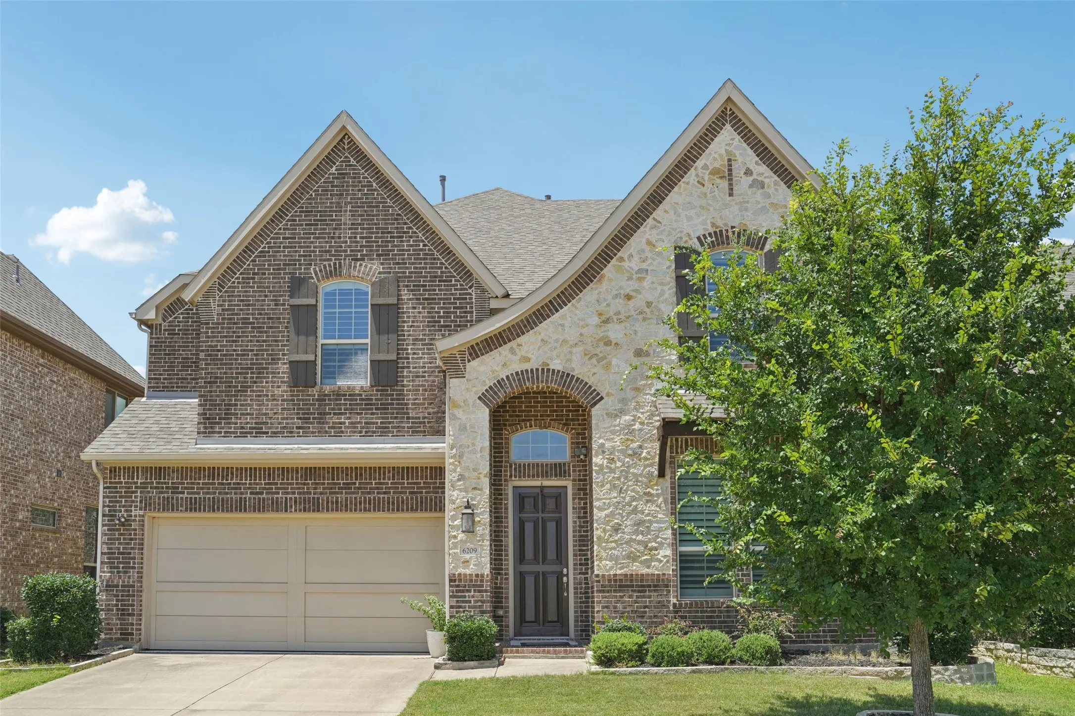 French country inspired facade featuring brick siding, concrete driveway, an attached garage, and roof with shingles