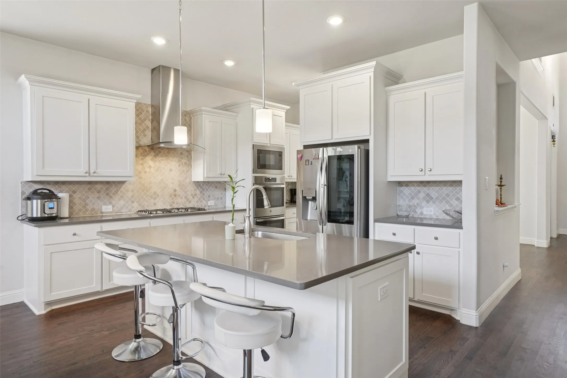 Kitchen featuring wall chimney exhaust hood, stainless steel appliances, decorative backsplash, a kitchen island with sink, and dark wood-style flooring