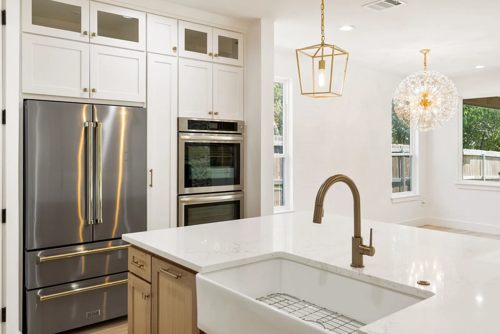 White cabinetry with glass-front accents, integrated double ovens, and a stainless steel refrigerator