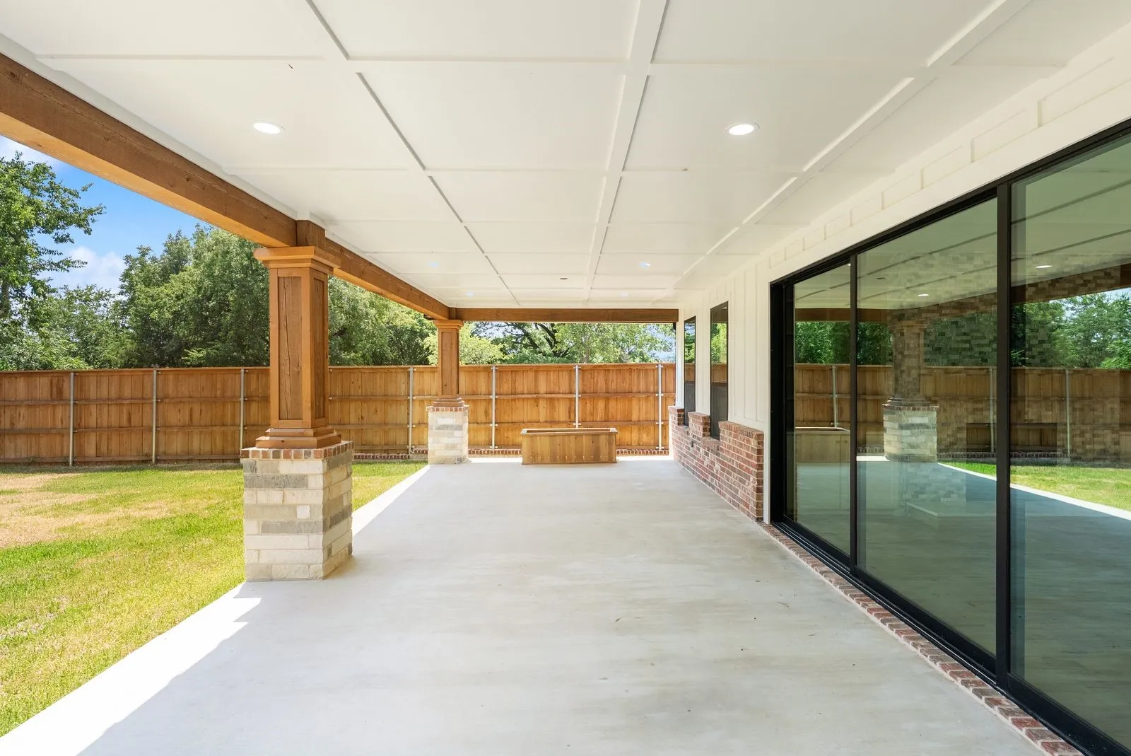 Covered patio with a coffered ceiling, wood-finish beams, brick and stone columns, and sliding glass doors