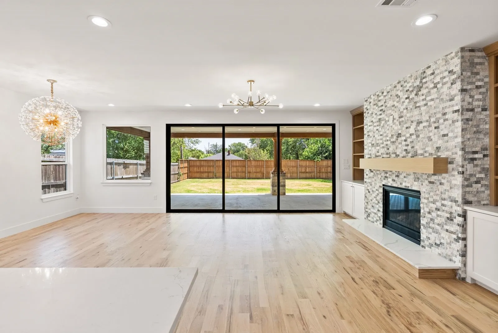 Hardwood flooring, a mosaic-tiled fireplace with a wood mantle, built-in shelving, and sliding glass doors opening to a backyard patio