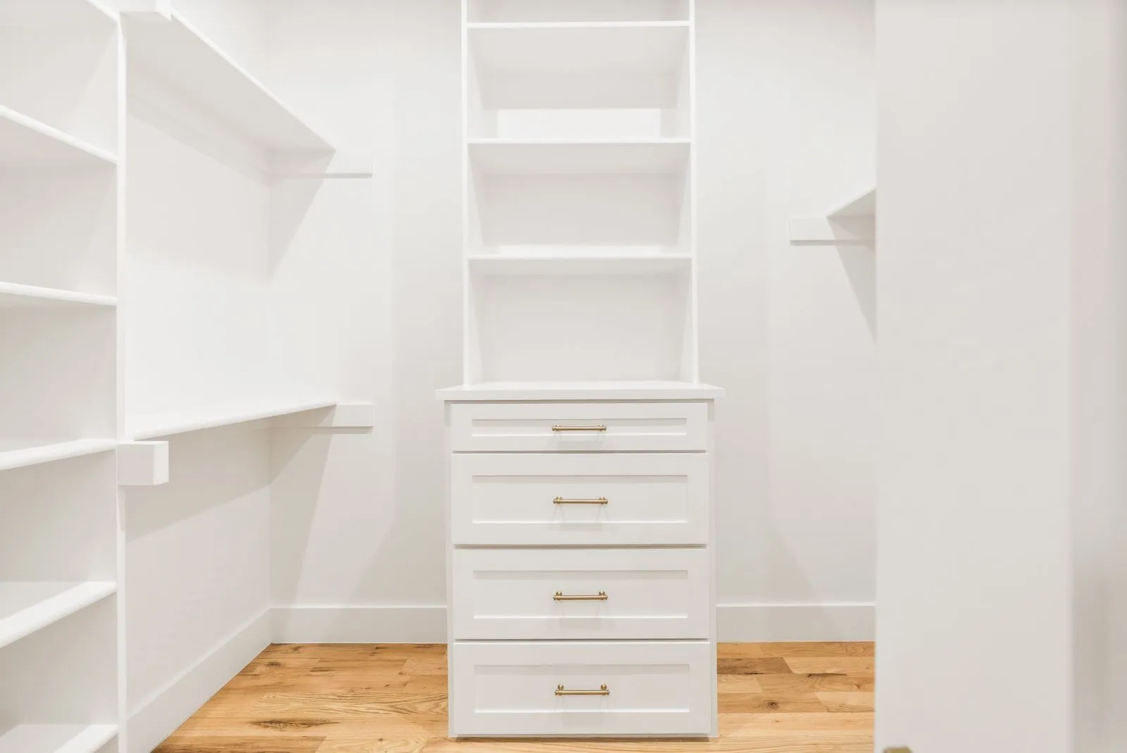 Built-in cabinetry with white shelving, drawer storage, and warm wood-finish flooring