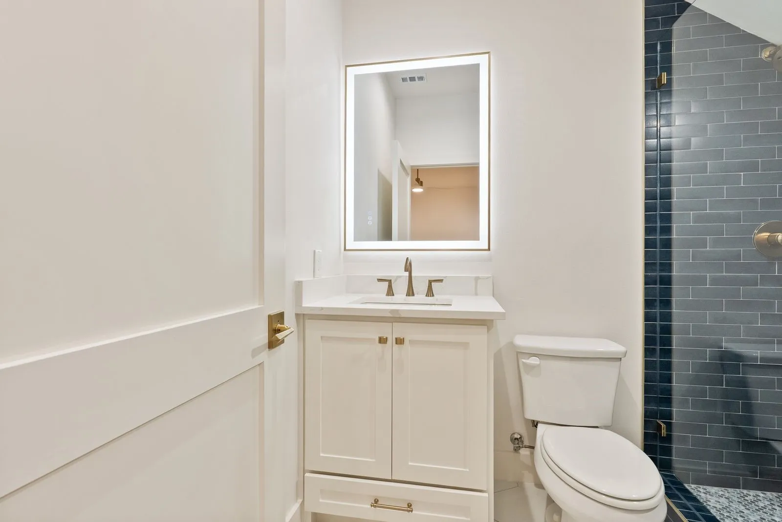 Vanity with a light-colored countertop, gold-tone hardware, and an illuminated mirror