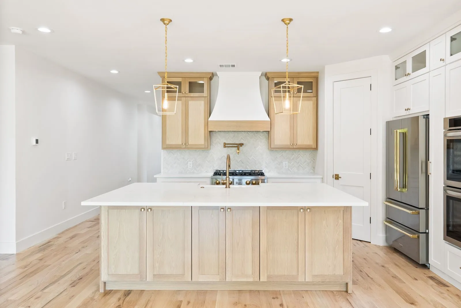 Kitchen featuring a large central island, light wood-finish cabinetry, stainless steel appliances, and brass-tone pendant lighting
