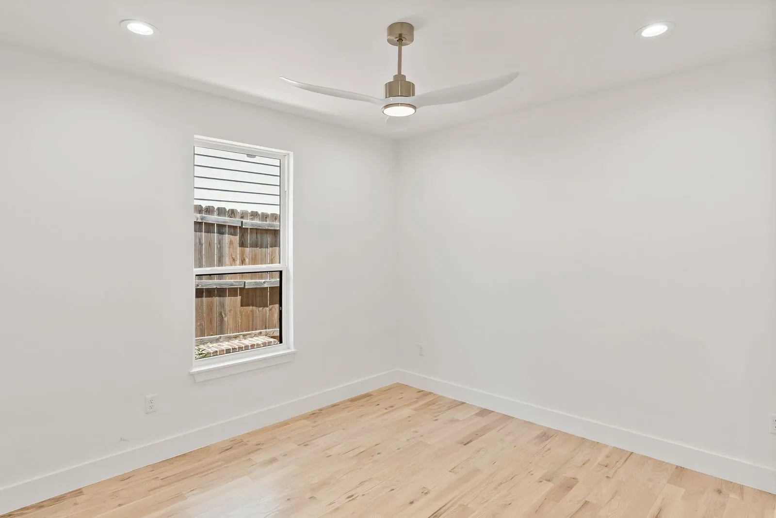 Recessed ceiling lighting, modern ceiling fan, wood-finish flooring, white trim, and a window with a wooden fence background