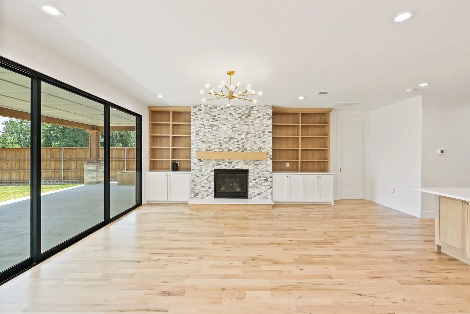 Hardwood flooring, expansive glass sliding doors, built-in shelving, stone-tiled fireplace, and a contemporary chandelier