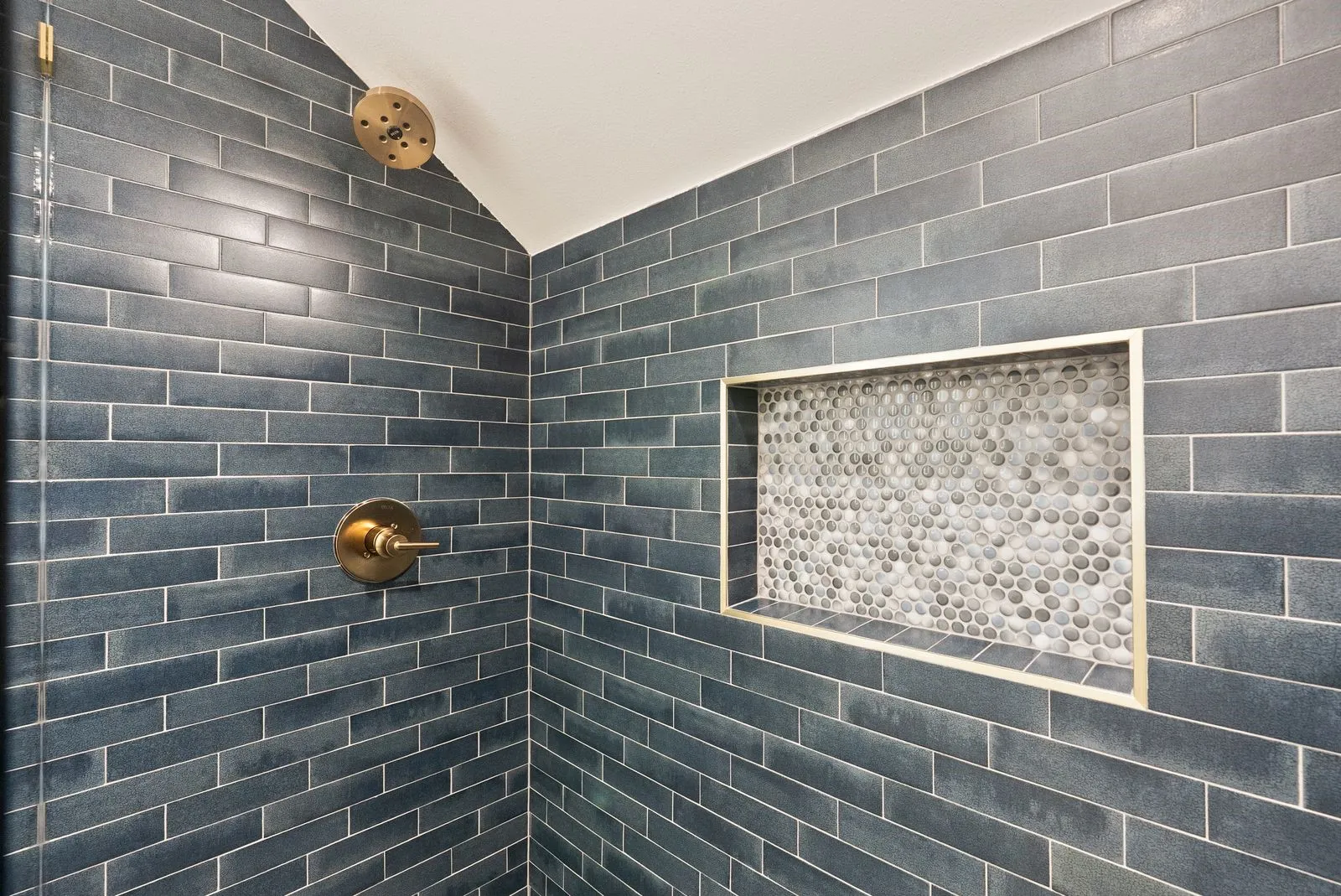 Shower with dark subway tile, brass fixtures, and a recessed niche featuring penny tile