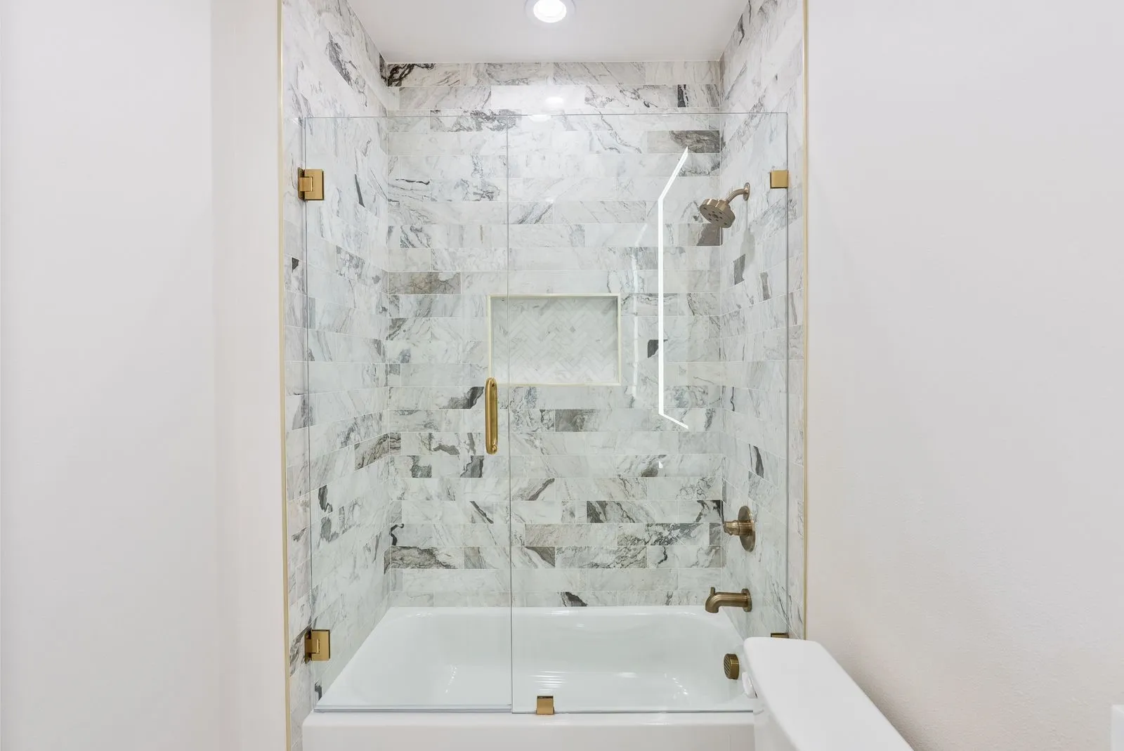 Bathtub with a glass shower enclosure, mosaic-tiled shower surround, recessed shower niche, and brass fixtures