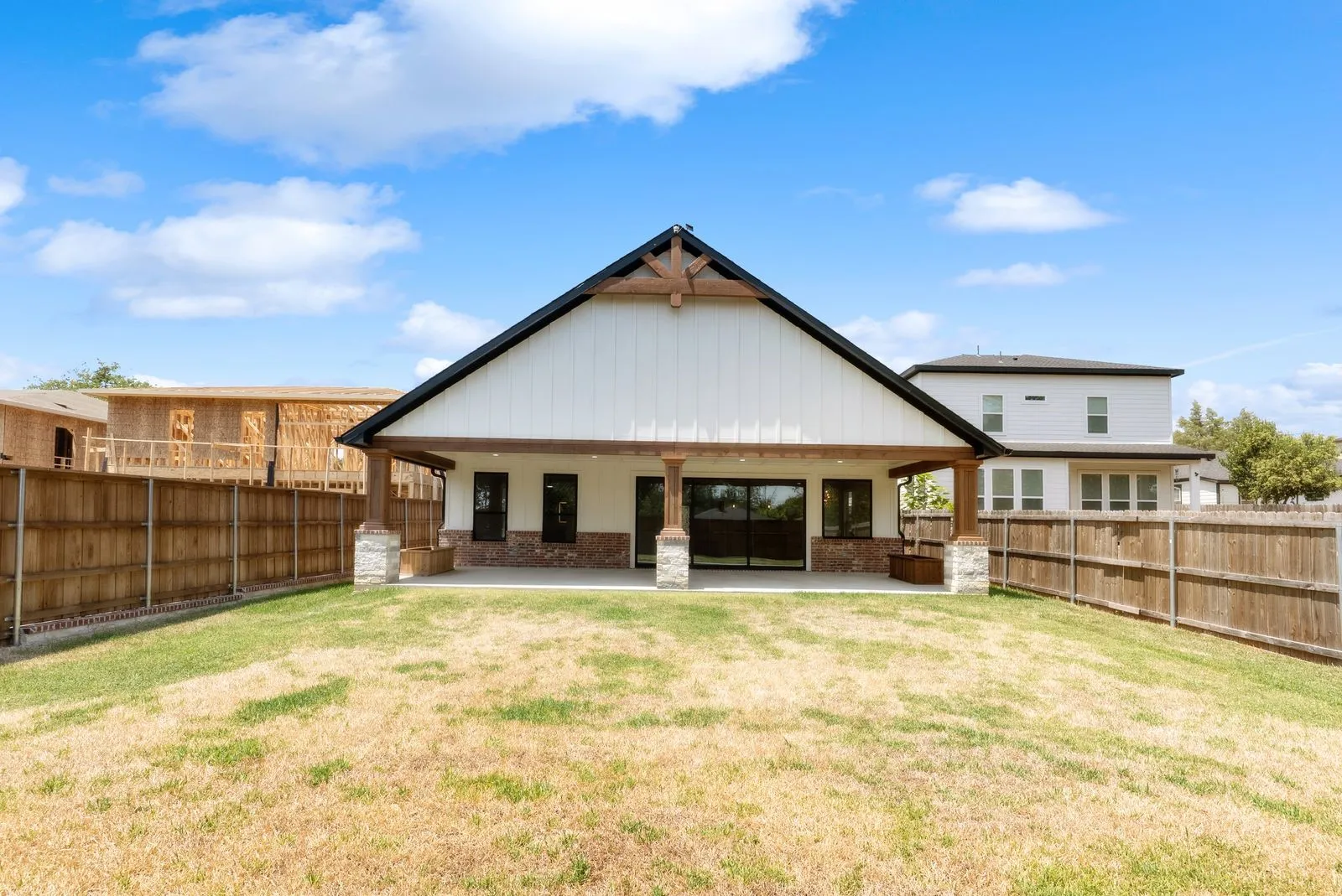 Spacious backyard featuring a large concrete patio, board and batten siding, substantial wood structural elements, stone columns, and wood privacy fencing